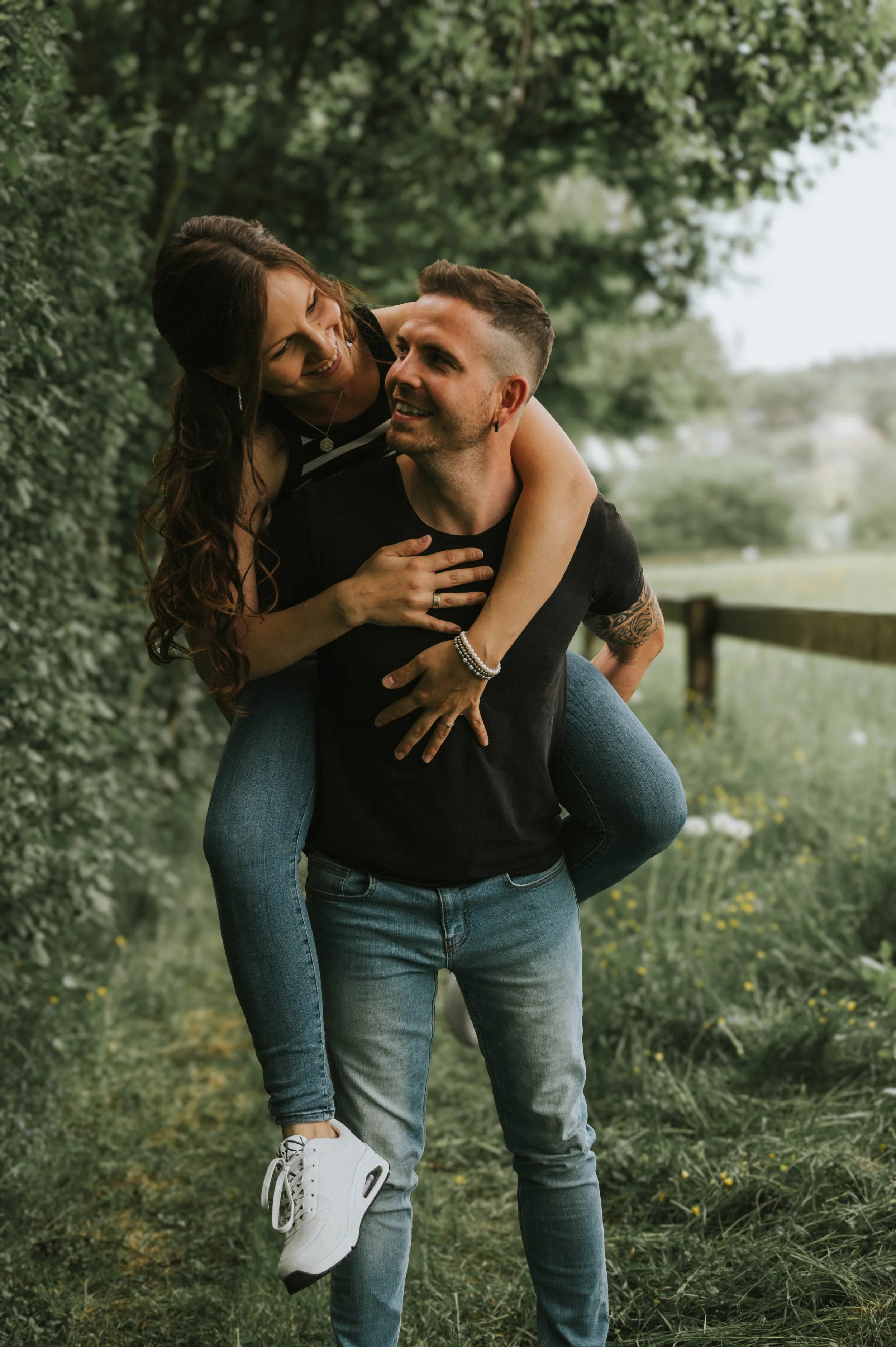 Ein lachendes Paar im Park, das Spaß miteinander hat, wobei der Mann das Mädchen auf seinem Rücken trägt.