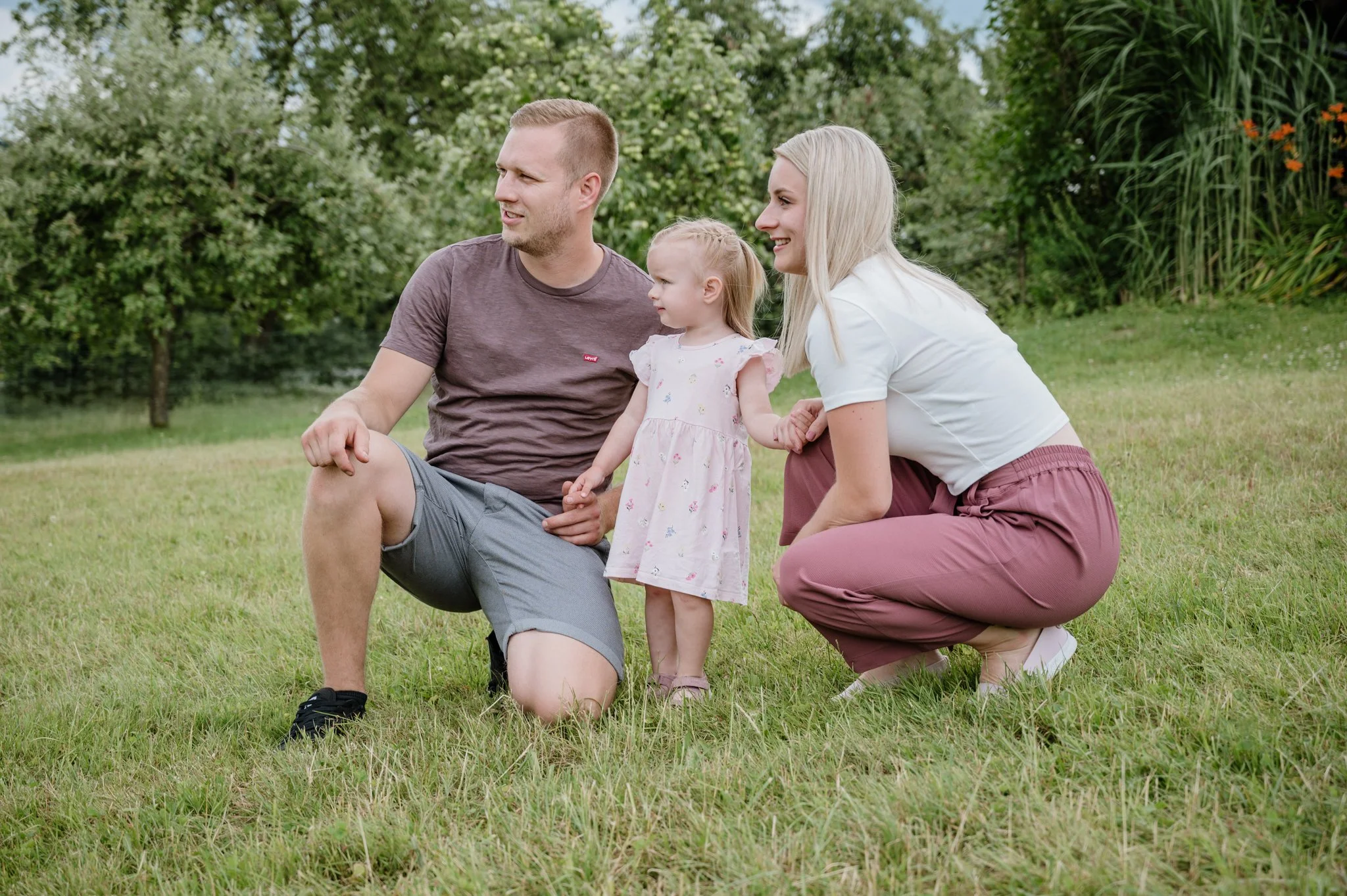 Familie mit zwei Erwachsenen und einem Kleinkind im Park, alle lachen und haben Spaß.