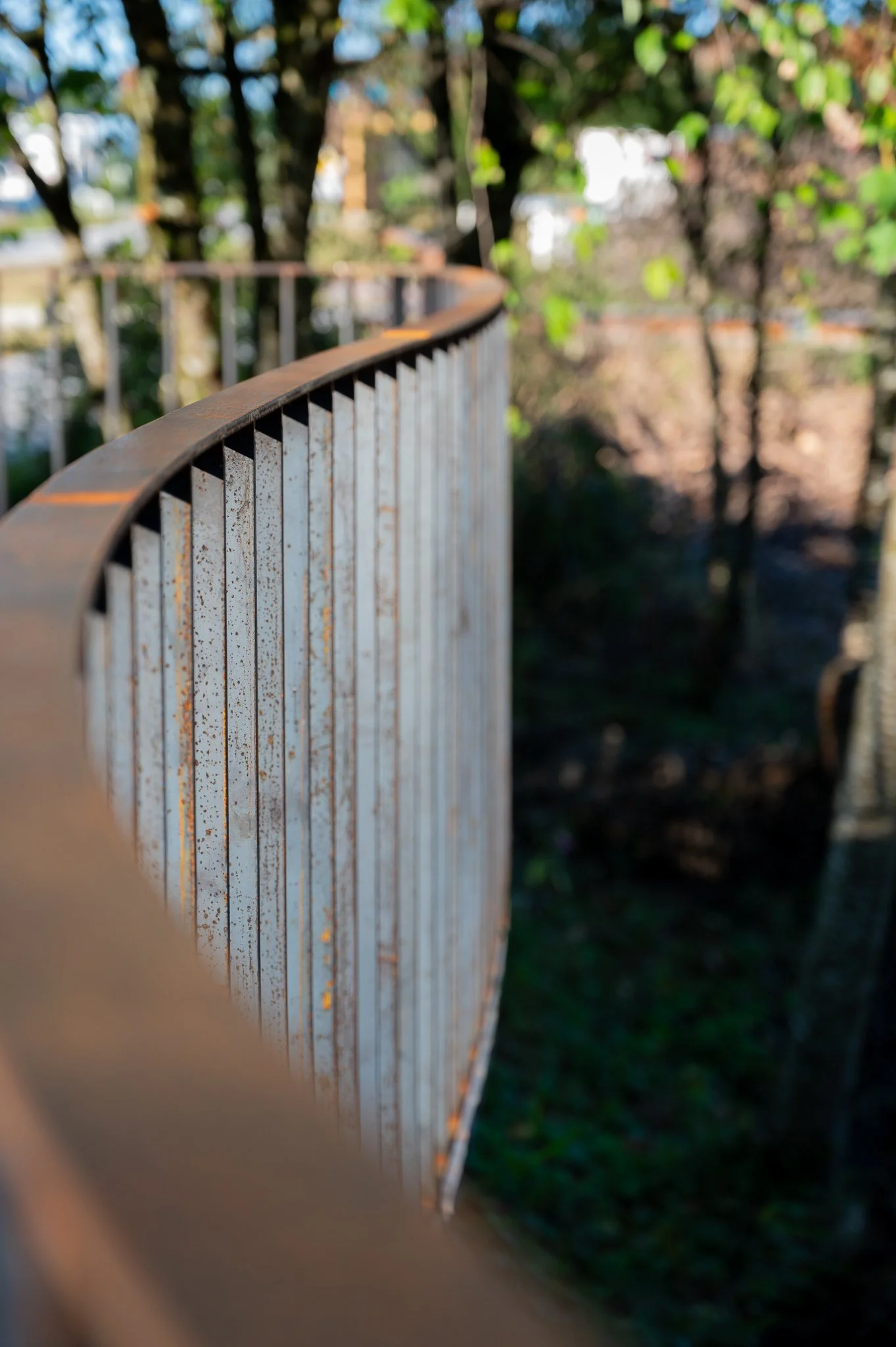 Nahaufnahme eines rostigen Metalzauns vor einem bewaldeten Hintergrund.