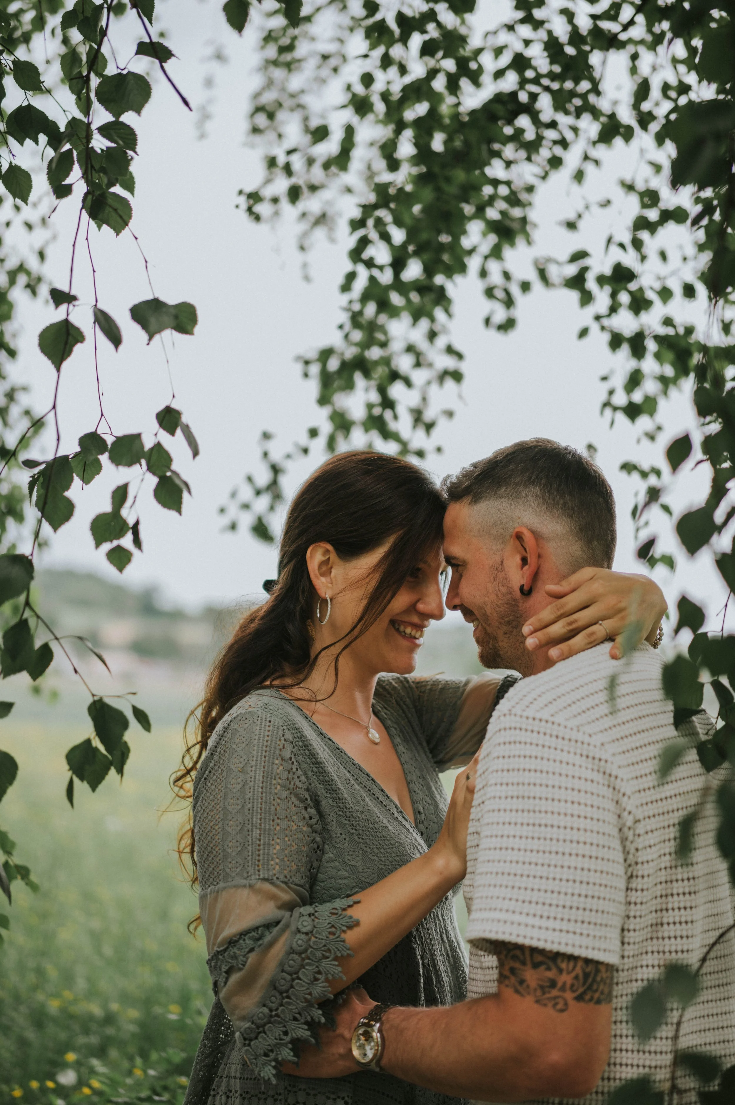 Ein Paar, das sich in einer Naturkulisse liebevoll gegenübersteht, mit umrahmenden Blättern über ihnen.