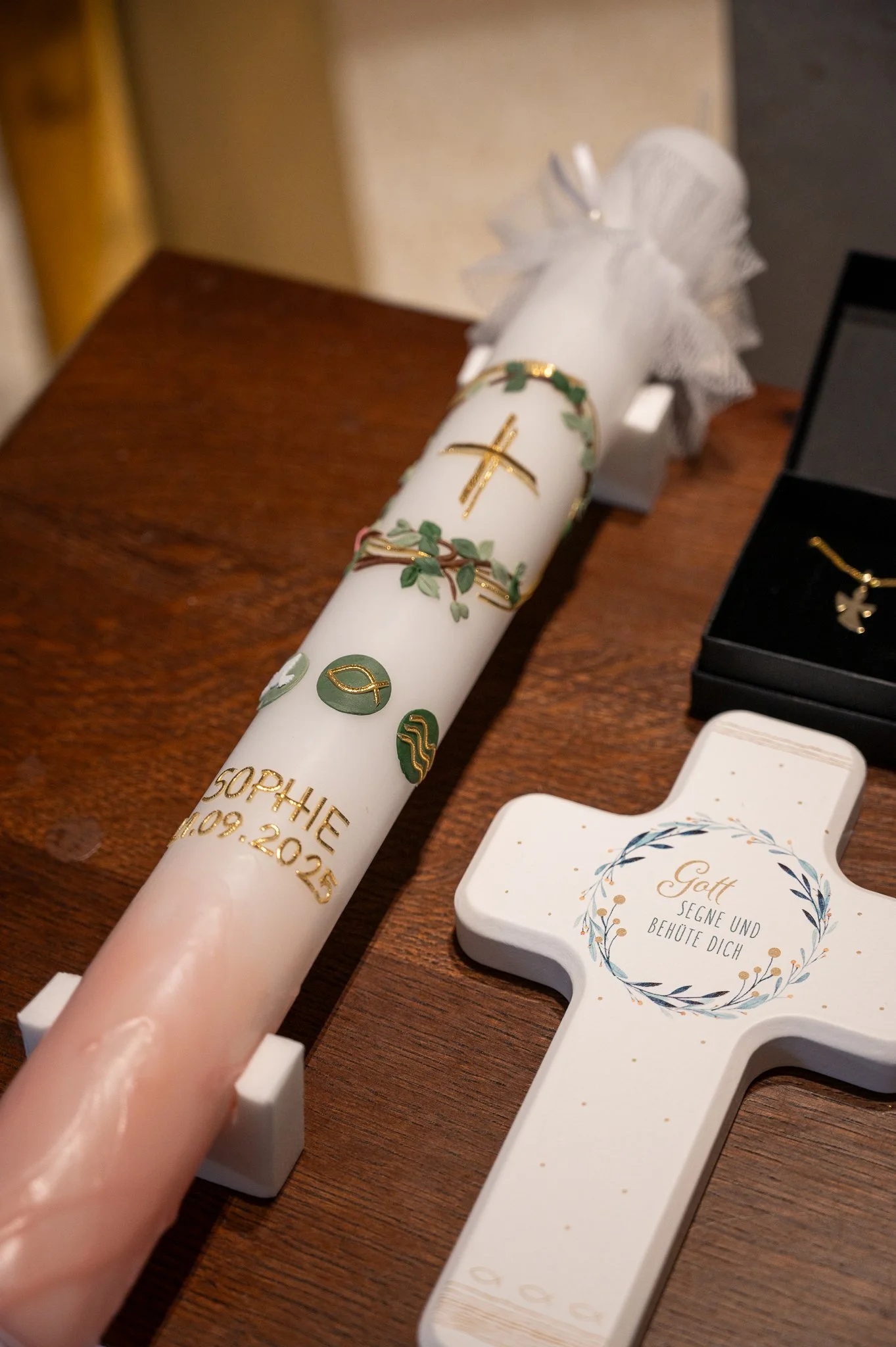 Ein Osterkerze mit Namen und Datum, eine weiße Osterkrippe mit der Aufschrift "Gott segne und behüte dich", weitere Schmuckstücke und Geschenke auf einem Holztablett.