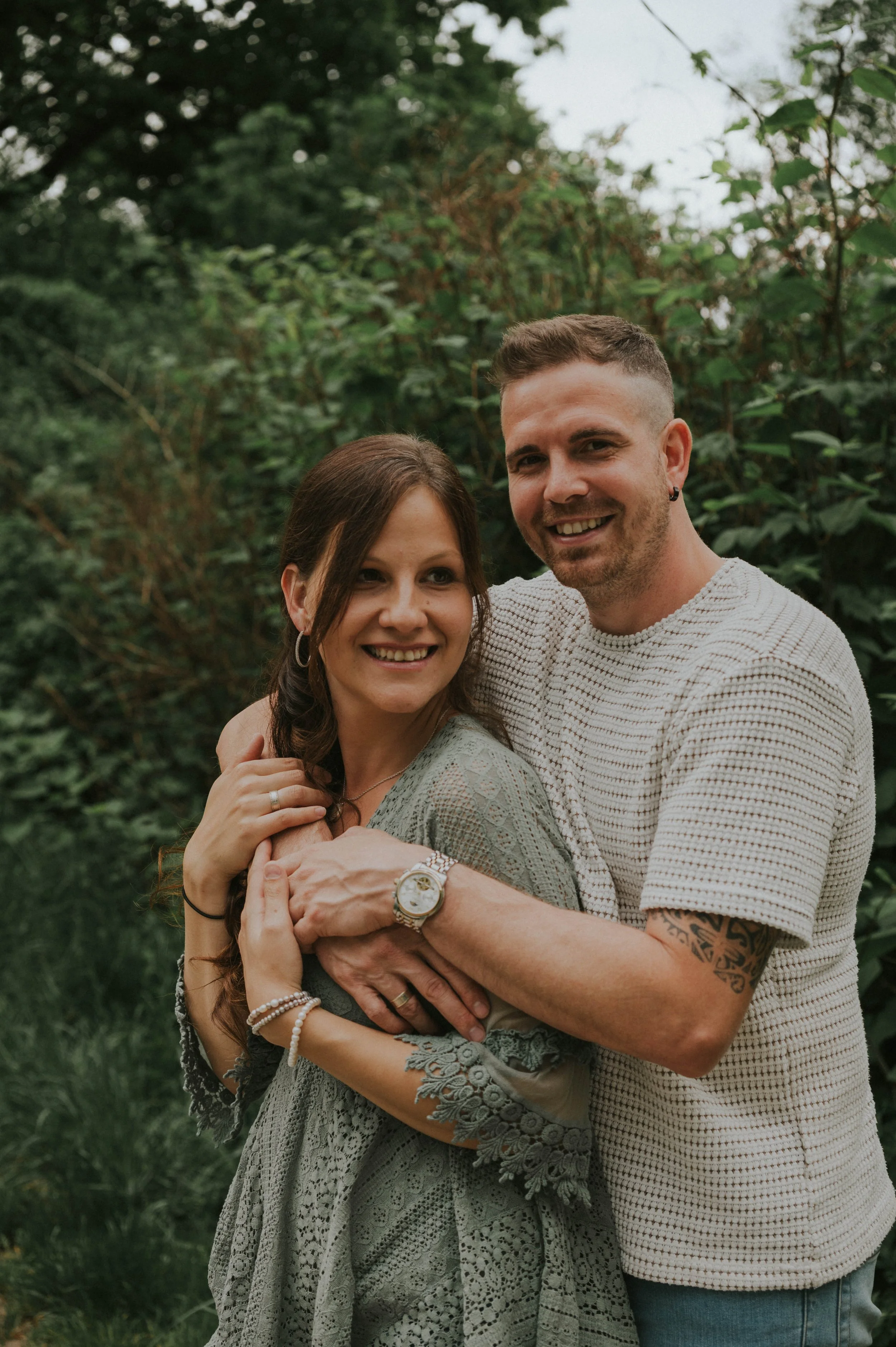 Ein lachendes Paar umarmt sich in einem grünen, bewaldeten Außenbereich.
