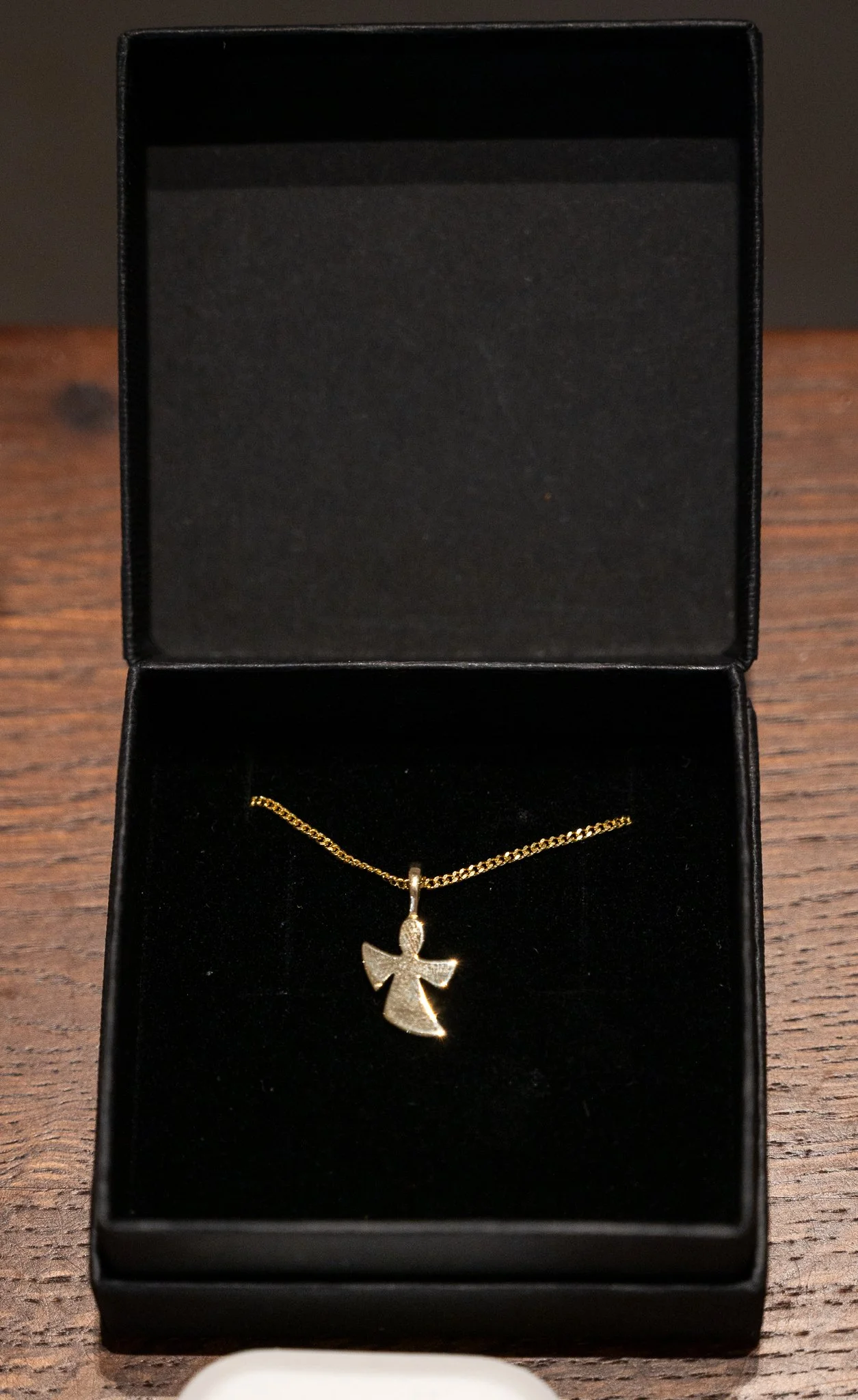 Goldener Halskette mit Anhänger in Form eines Engels in einer schwarzen Geschenkbox auf einem Holztisch.