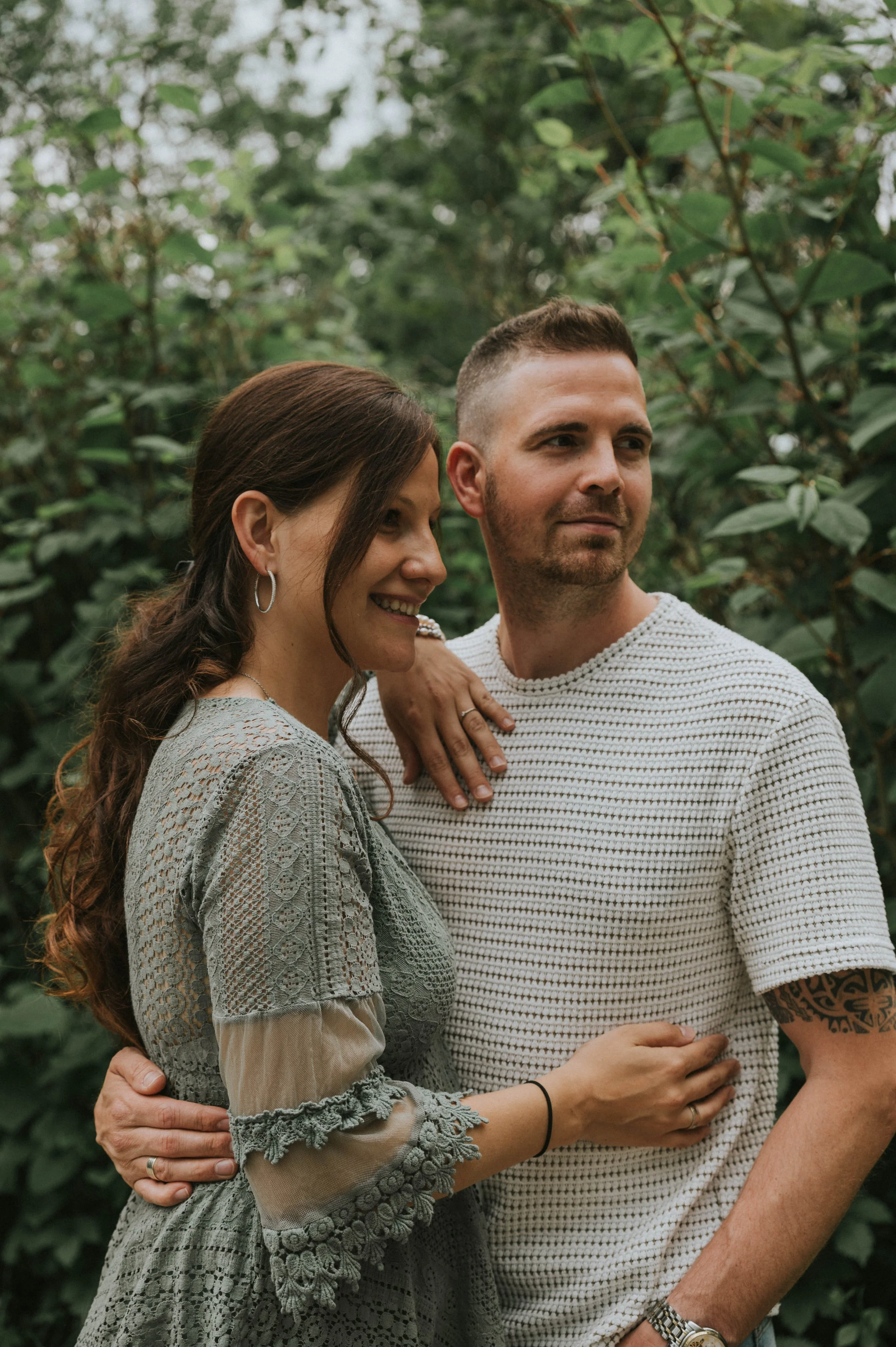 Ein Paar steht eng beieinander in einem grünen Garten, lächelt und posiert für die Kamera.