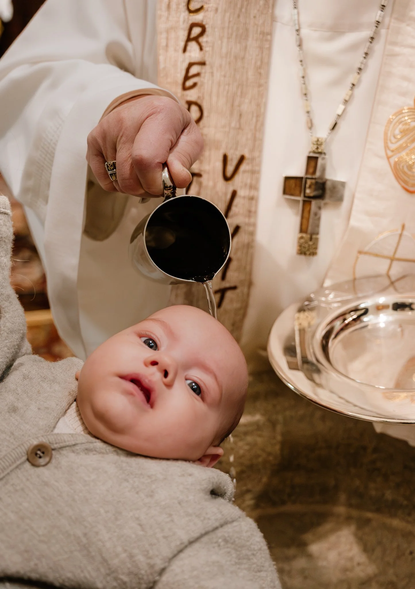 Ein Baby wird von einer Person mit einer kleinen Schöpfkelle mit Wasser begossen.