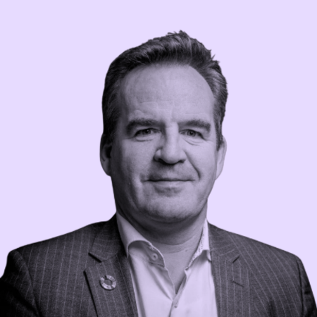 Portret van een man in een pak, met een lichte achtergrond.