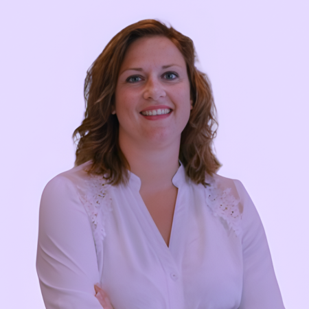 Vrouw met wapperend bruin haar, witte blouse, lachend, lichte achtergrond.