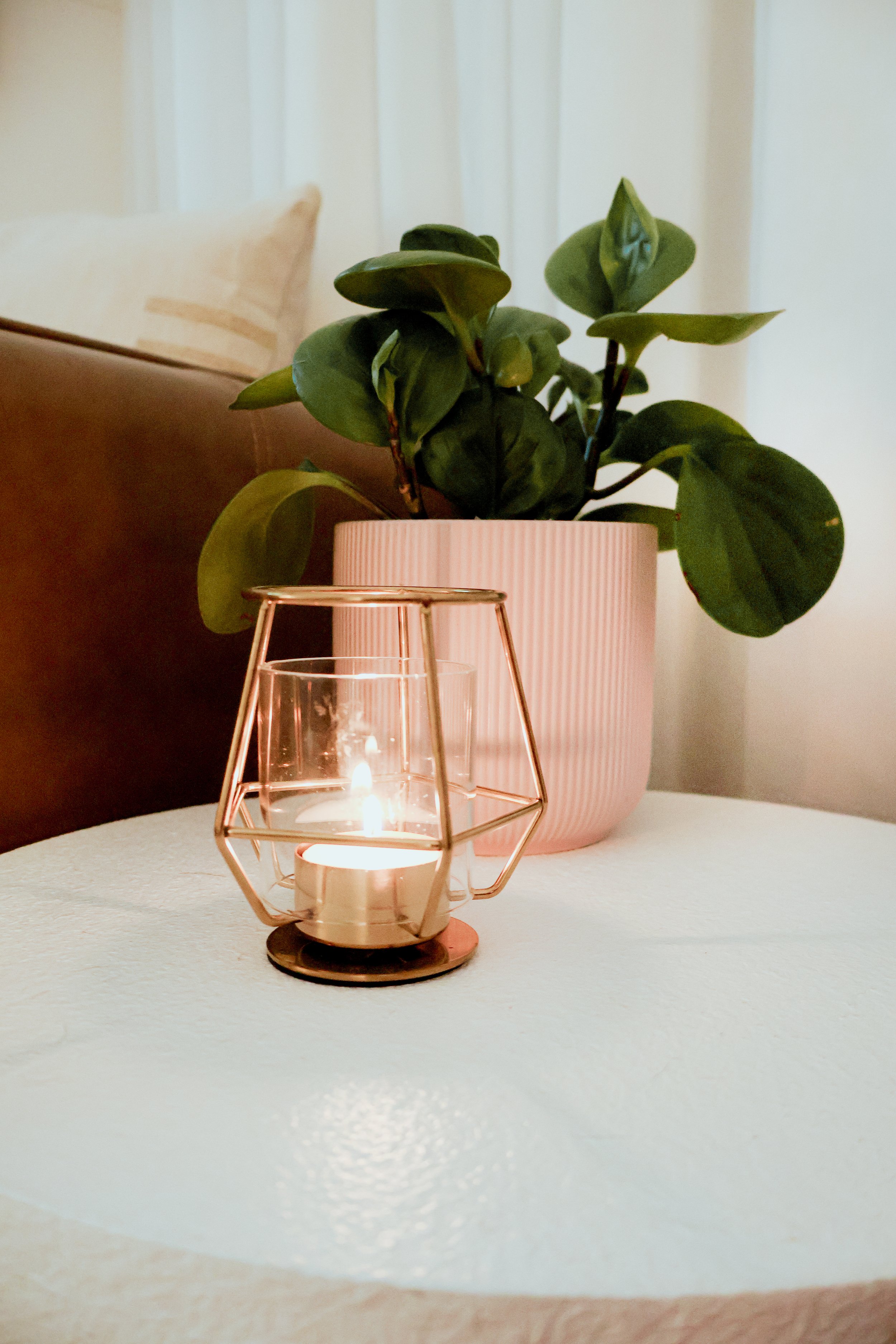 A table with a pink potted plant and a lit candle in a rose gold holder.