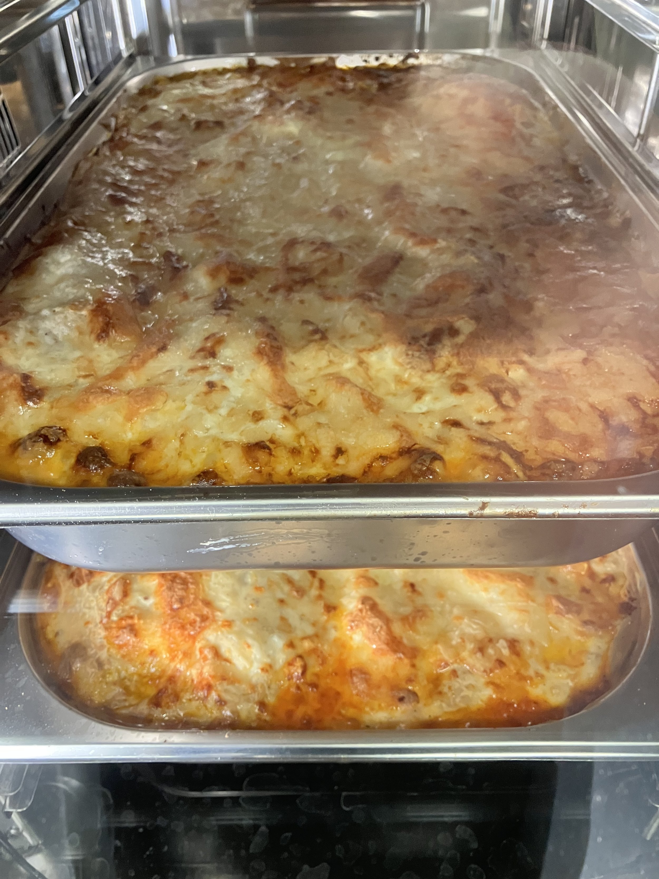 Twee metalen schalen met versgebakken lasagne, rijk gevuld met vlees, tomatensaus en perfect gesmolten kaas, rechtstreeks uit de oven. Een ambachtelijke bereiding die vakmanschap, authenticiteit en culinaire kwaliteit weerspiegelt ideaal voor profe