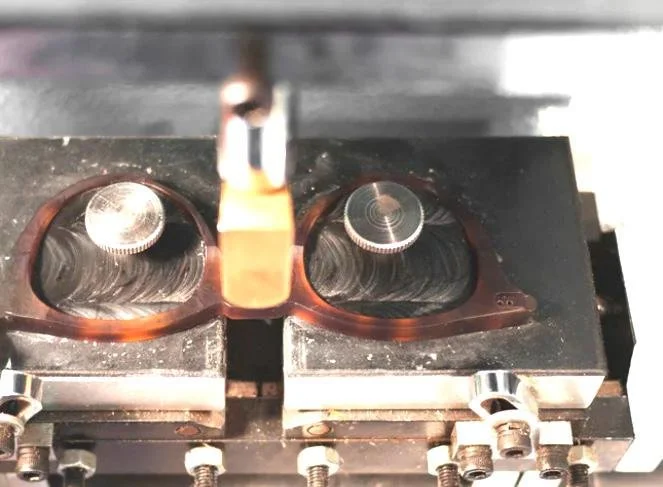 Close-up image of a laboratory instrument with two lenses and a metallic component in the center, mounted on a black base with screws.