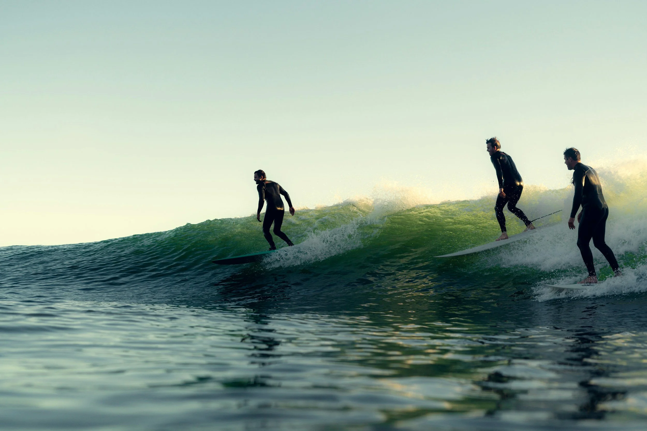 Three surfers riding a wave in the ocean during daytime.