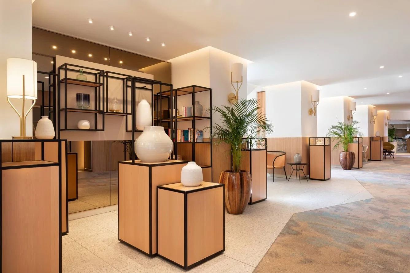 Polished hotel lobby with modern decor, potted plants, and decorative vases on black-framed display shelves.
