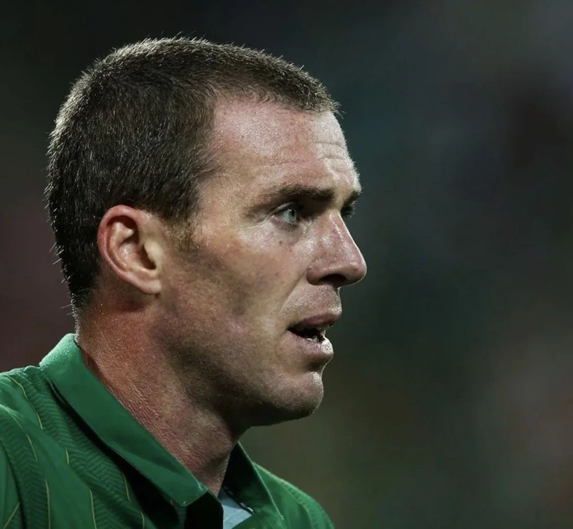 Close-up of a male soccer player with short dark hair, wearing a green jersey, on the field.