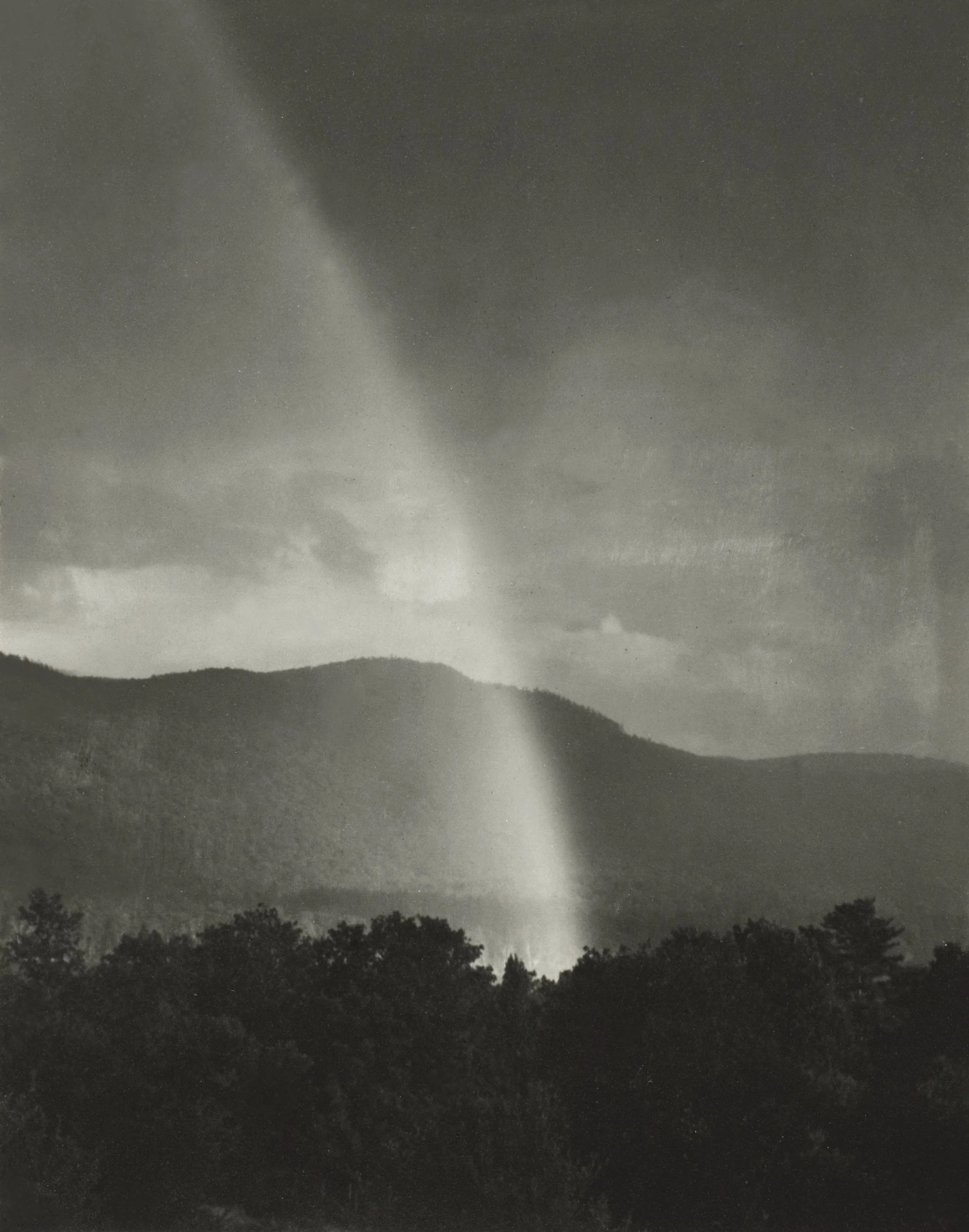 A black and white photograph of a natural landscape with hills, trees, and a cloud-filled sky. A bright, vertical lightning bolt appears to strike from the clouds to the ground.