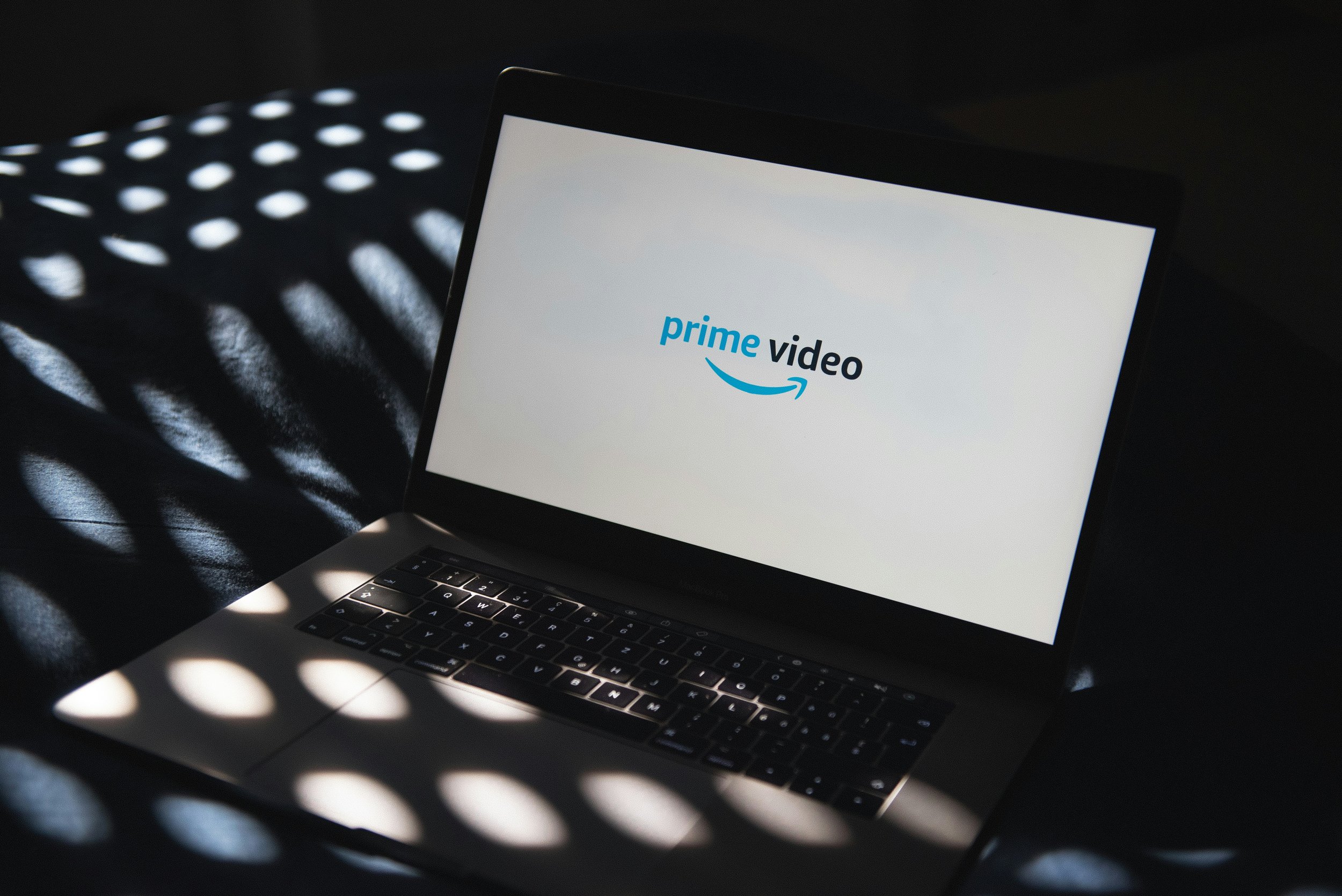 Laptop displaying the Amazon Prime Video logo on the screen, with light shadows creating circular patterns on the keyboard and surface.
