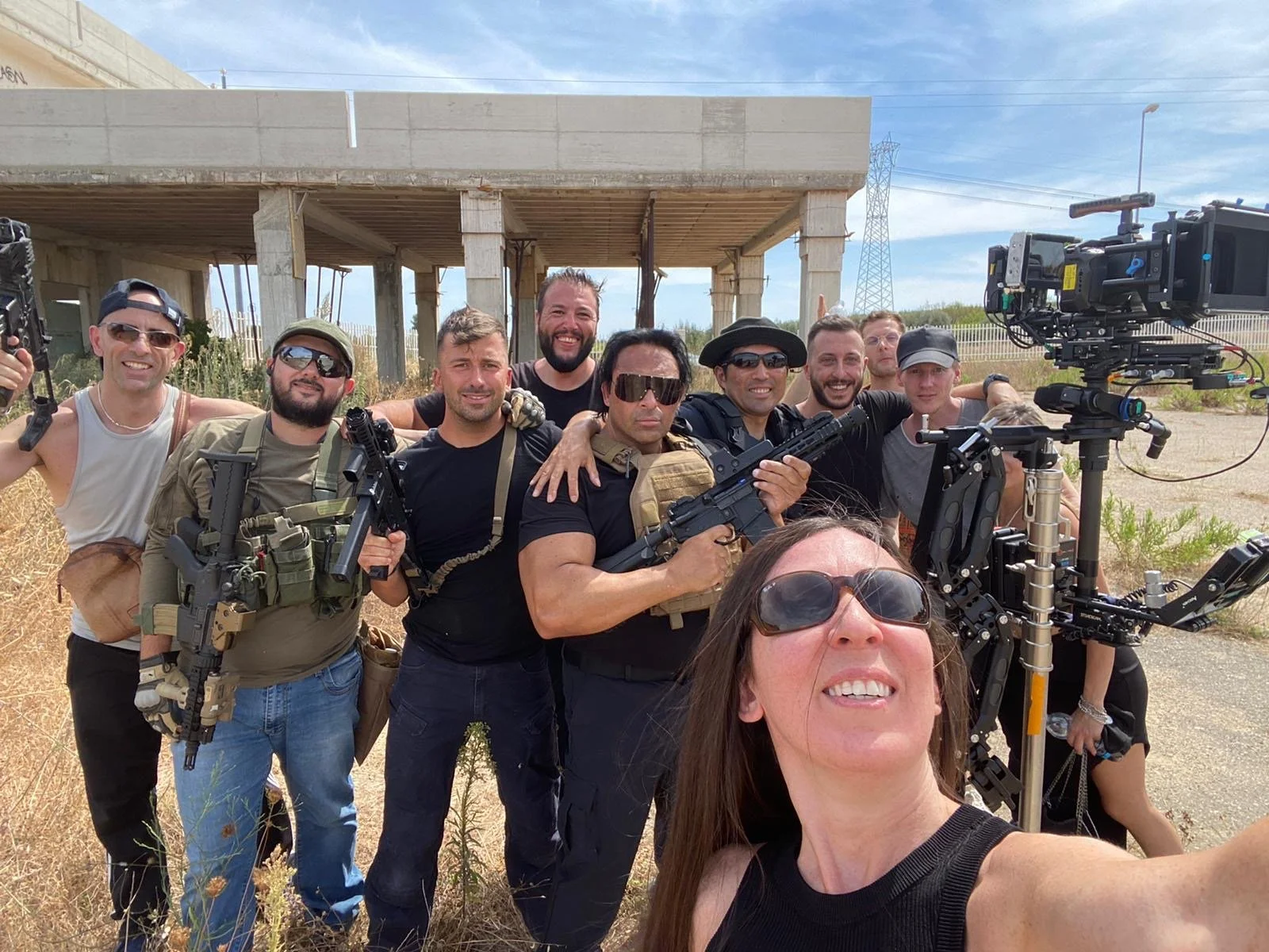 Group of people on set with film equipment outdoors under a partially constructed building.