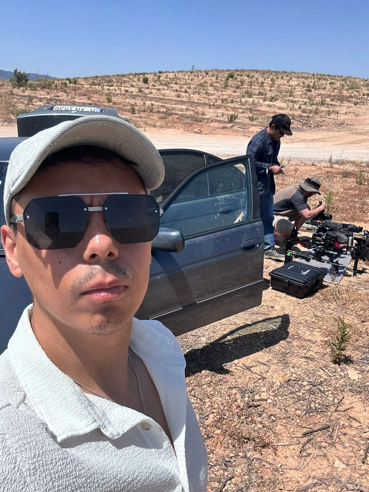 Man taking a selfie in a desert with filming equipment and crew in the background.
