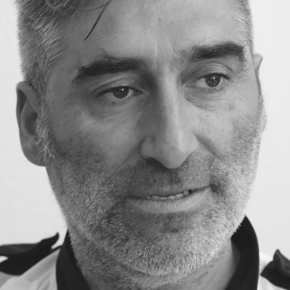 Close-up black and white photograph of a middle-aged man with gray hair and beard, looking slightly to the right.