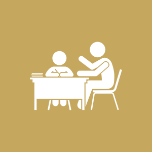 An adult reading a book to a child at a desk in a classroom.