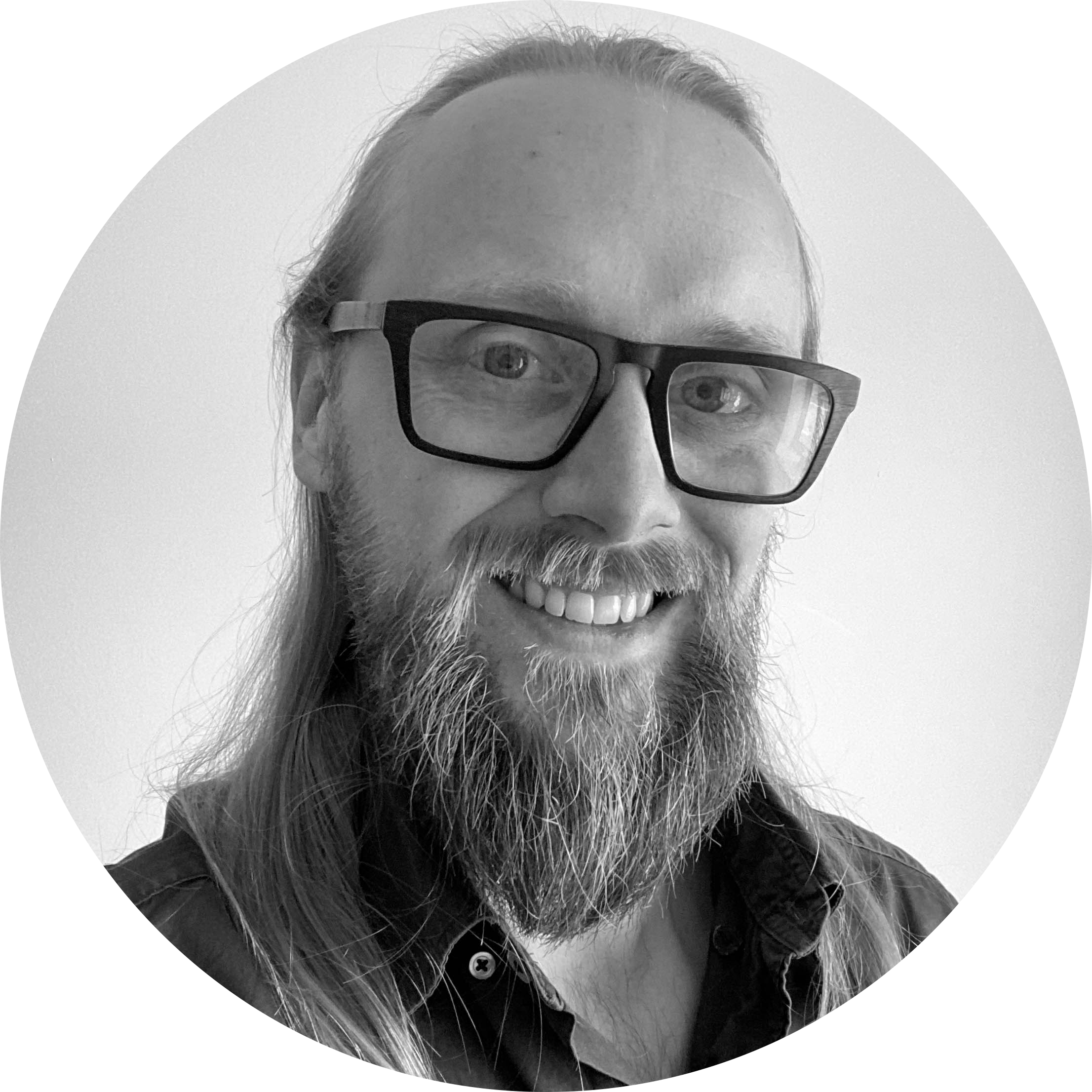 Black and white photo of a smiling man with long hair, beard, and glasses, wearing a dark shirt.
