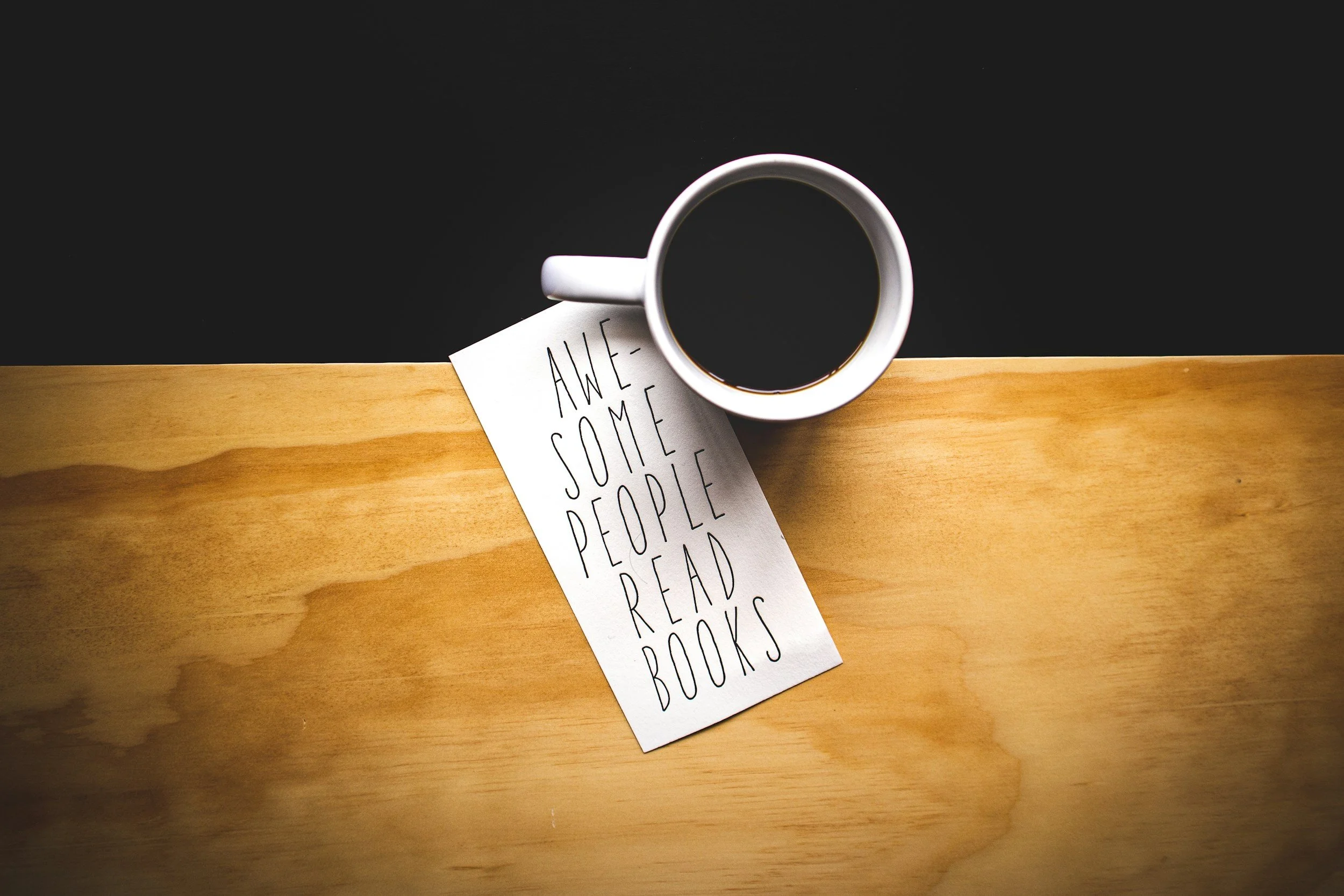 Mug of coffee balancing on a table on a postcard that says Awesome People Read Books