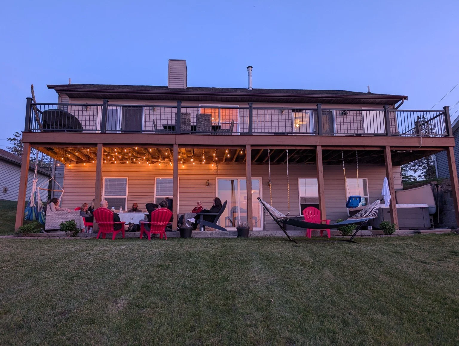 Lakefront vacation rental on Houghton Lake at dusk, with a family reunion group gathered on the covered patio