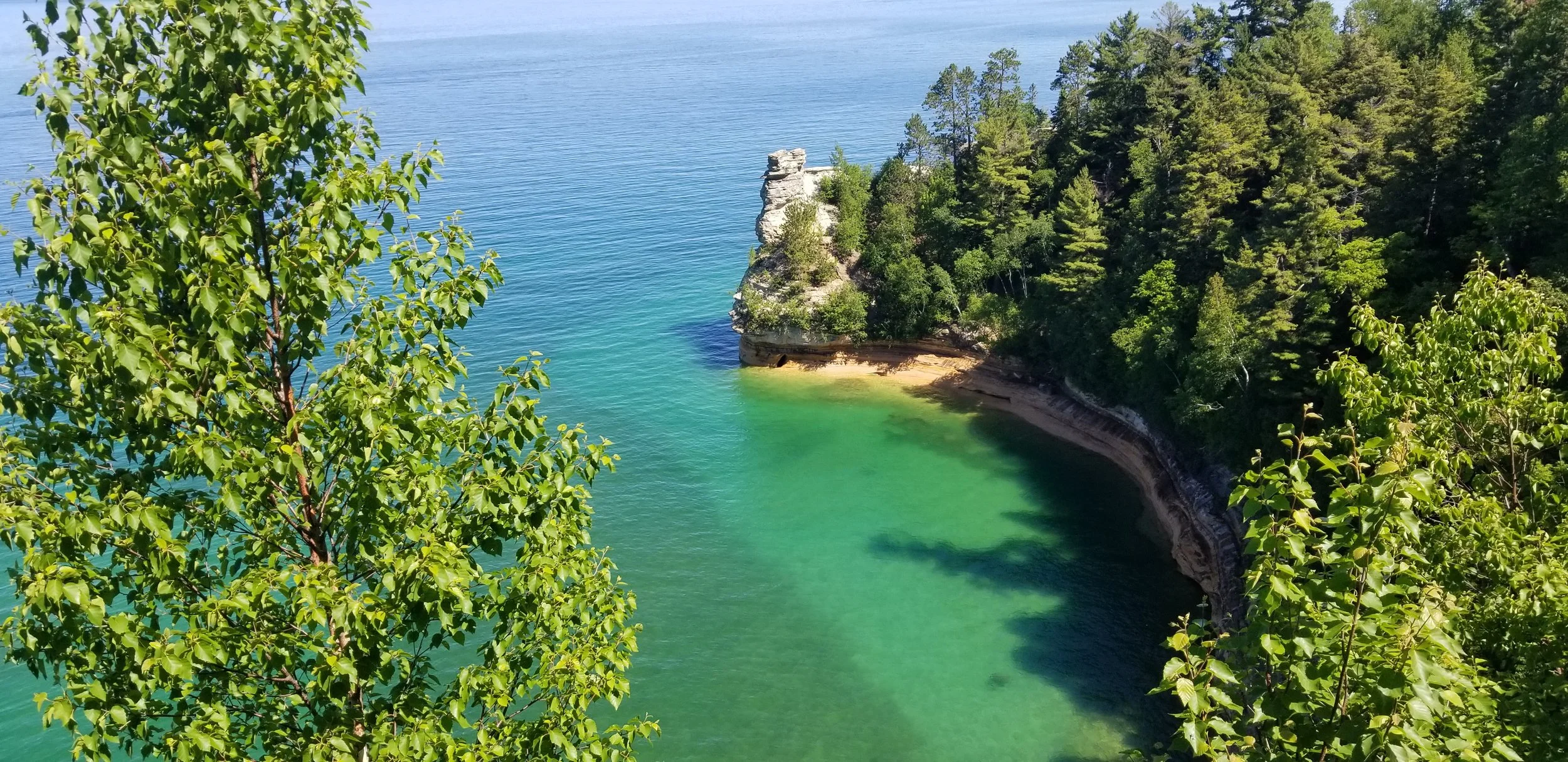 The iconic Pictured Rocks National Lakeshore on  Lake Superior — one of the most breathtaking  kayaking destinations in all of Michigan featuring  towering sandstone cliffs and impossibly clear  turquoise waters