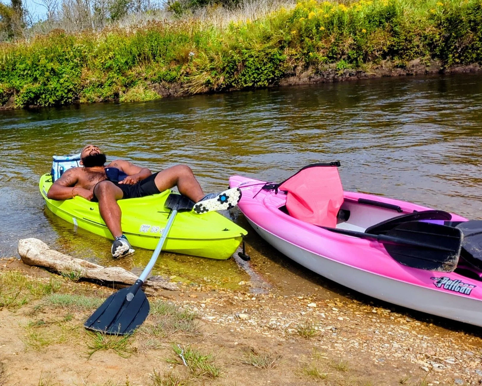 A kayaker taking a relaxing nap in a bright yellow  kayak on a peaceful Northern Michigan river bank -  the perfect definition of a lazy paddle day up north
