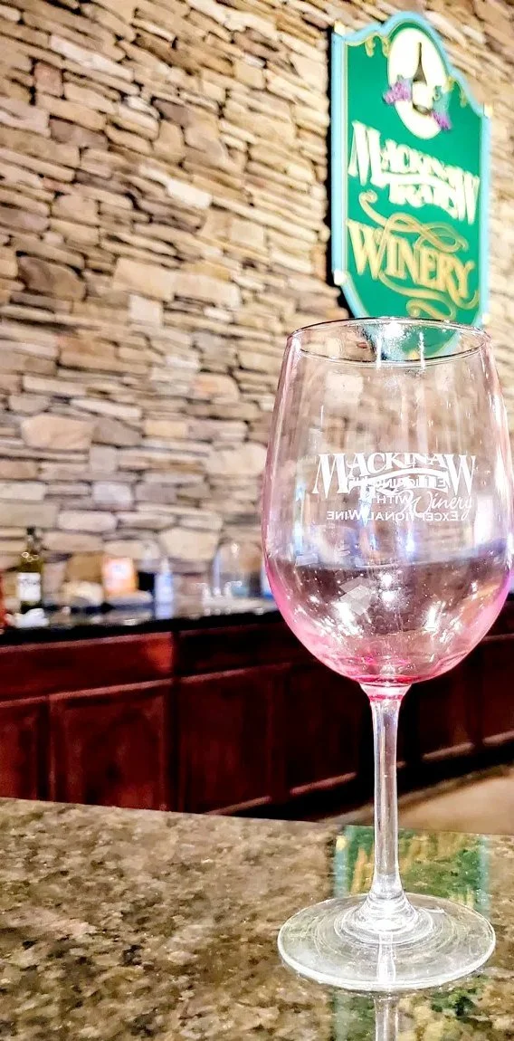 Etched Mackinaw Trail Winery glass on the granite tasting bar in front of the winery's green sign