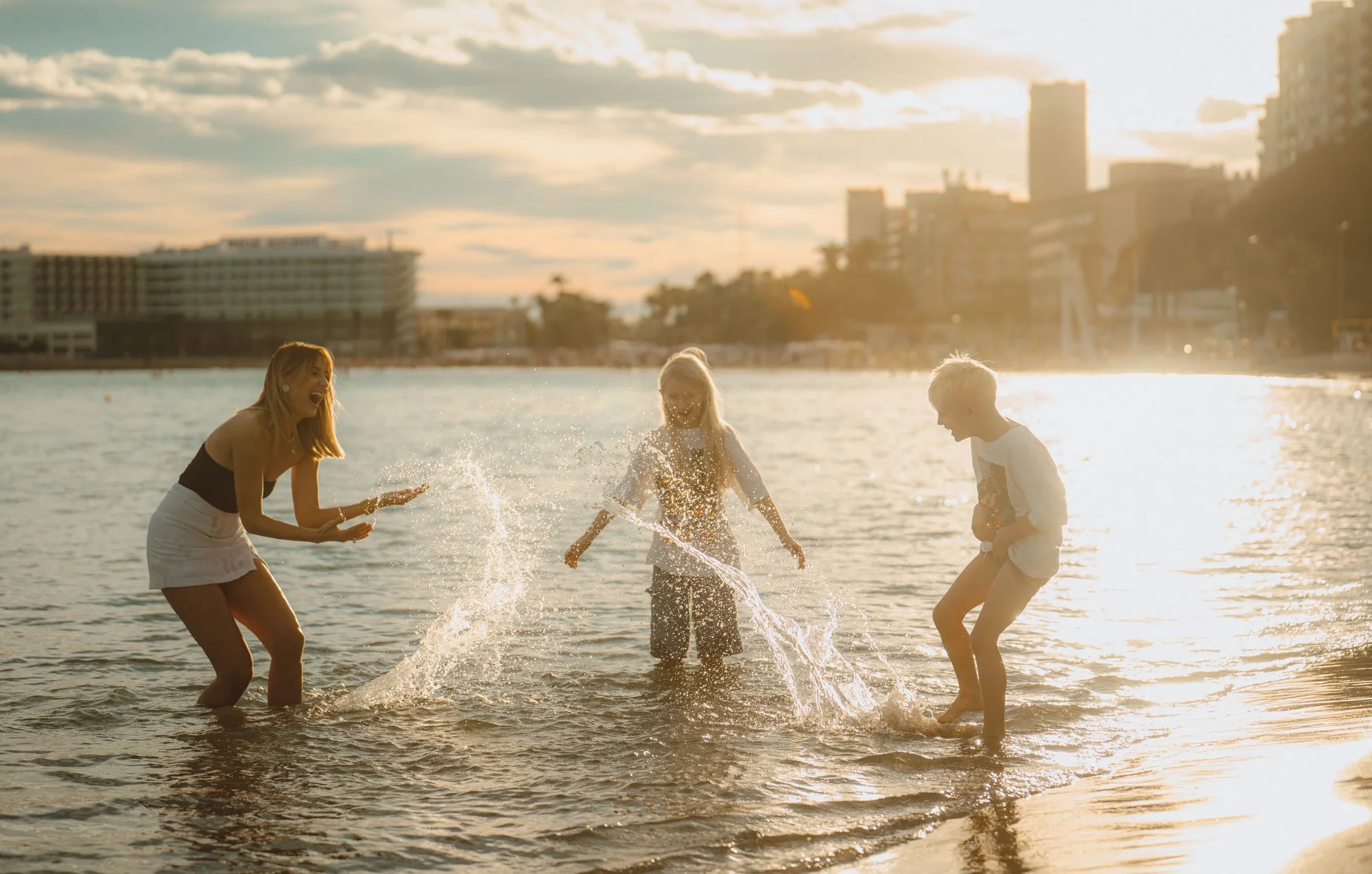 Three children playing and splashing water in the ocean during sunset.