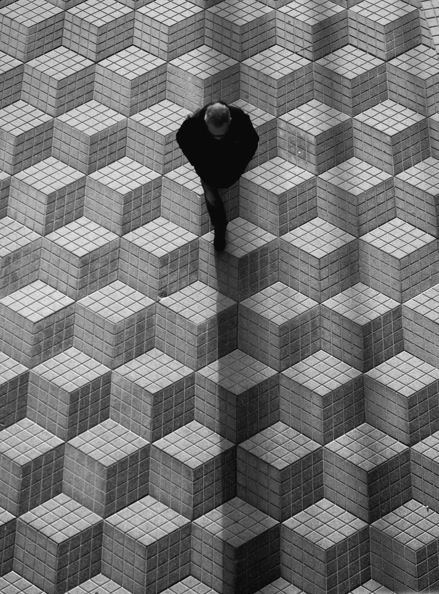 A person walking on a tiled floor with a geometric pattern of cubes in black and white.