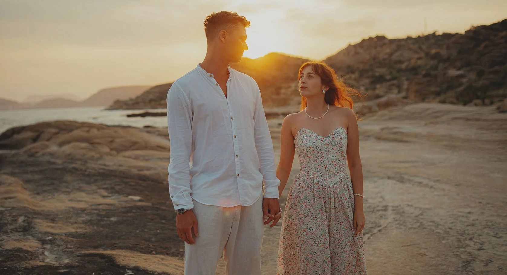 Para stoi na skalistym terenie w pobliżu zbiornika wodnego o zachodzie słońca, trzymając się za ręce i patrząc na siebie. Alicante