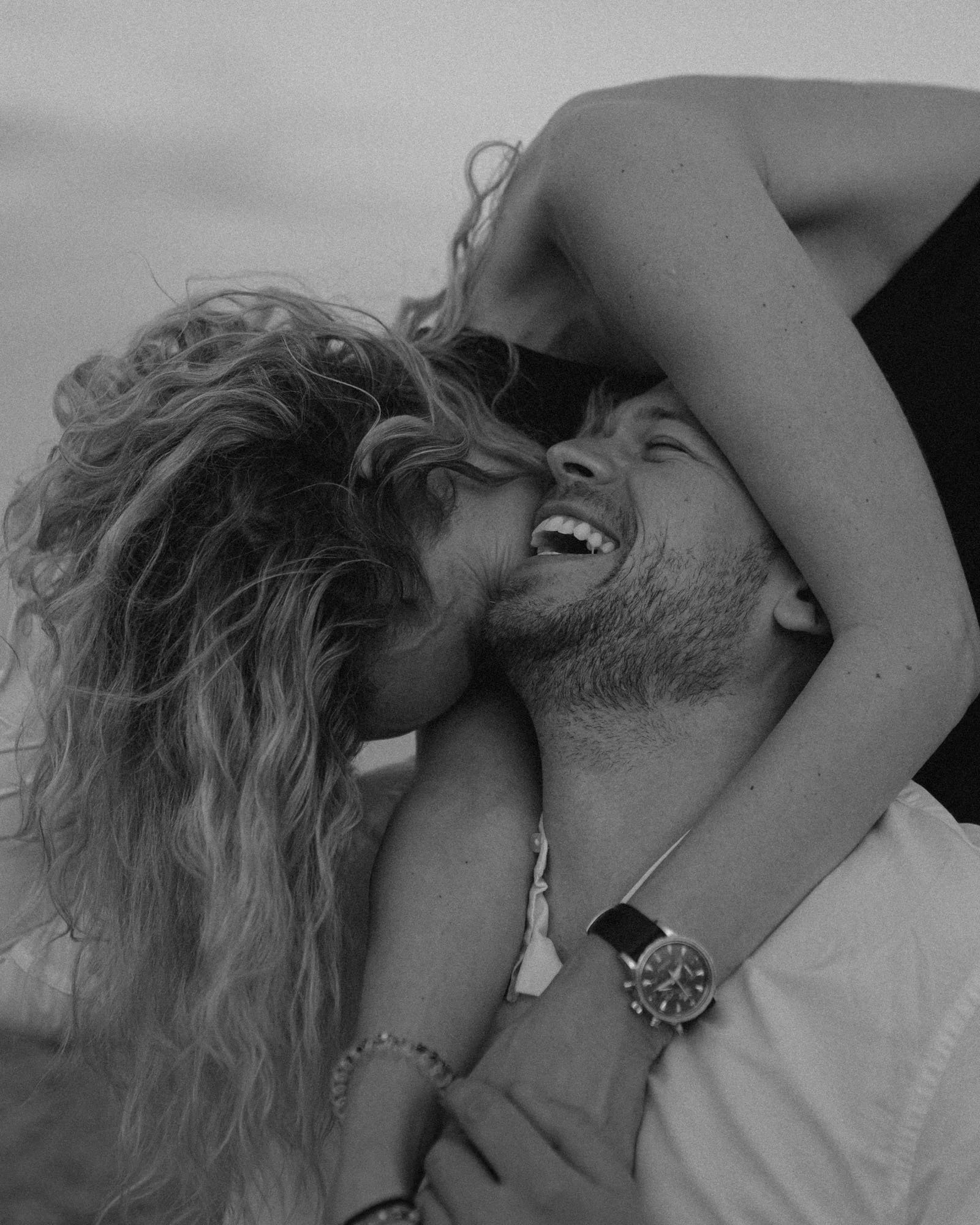 A couple sharing a joyful moment, with the woman kissing the man on the cheek and the man laughing, both lying close together. Alicante photoshoot