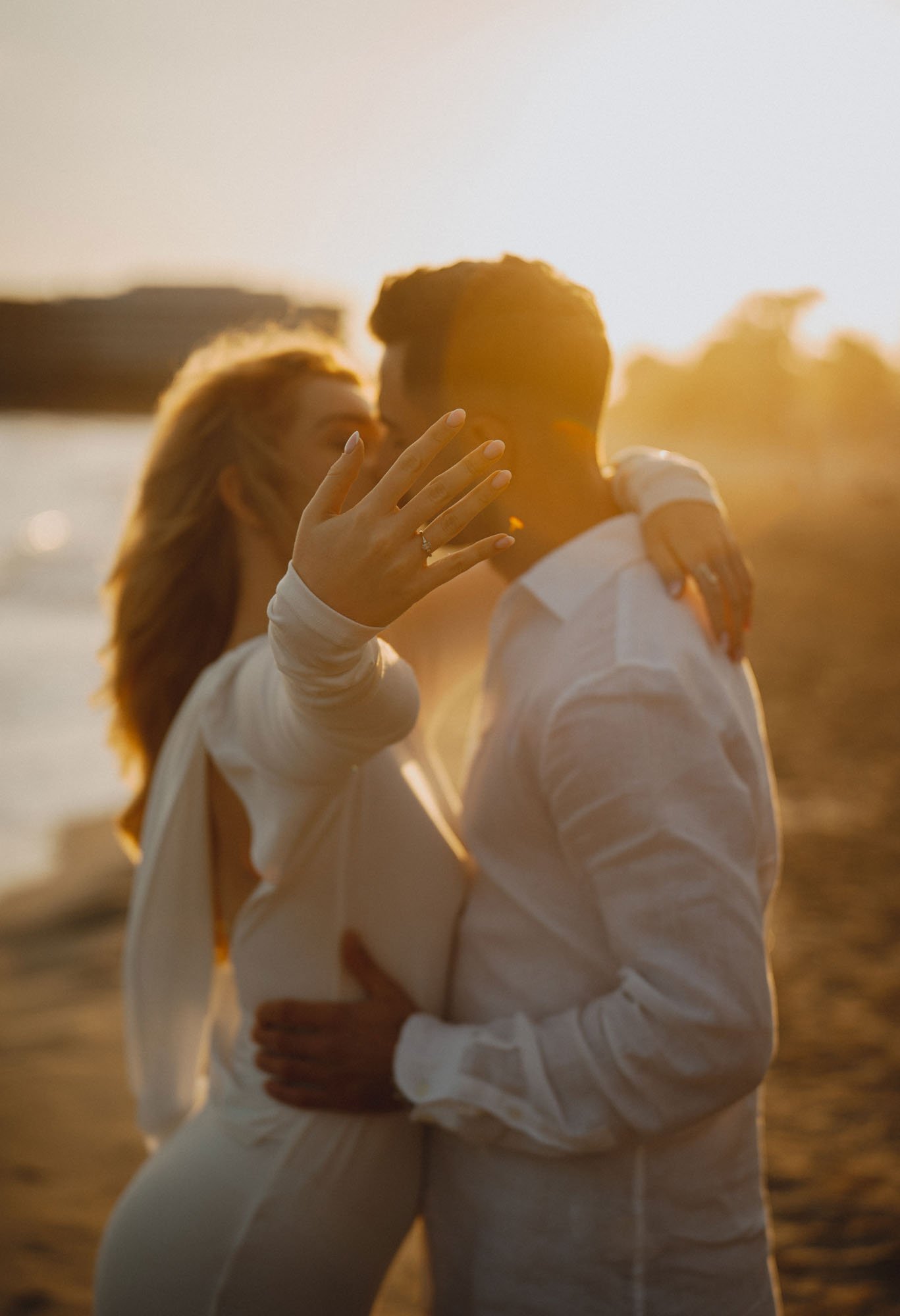 A couple standing close together during sunset, with the woman's hand showing an engagement ring.