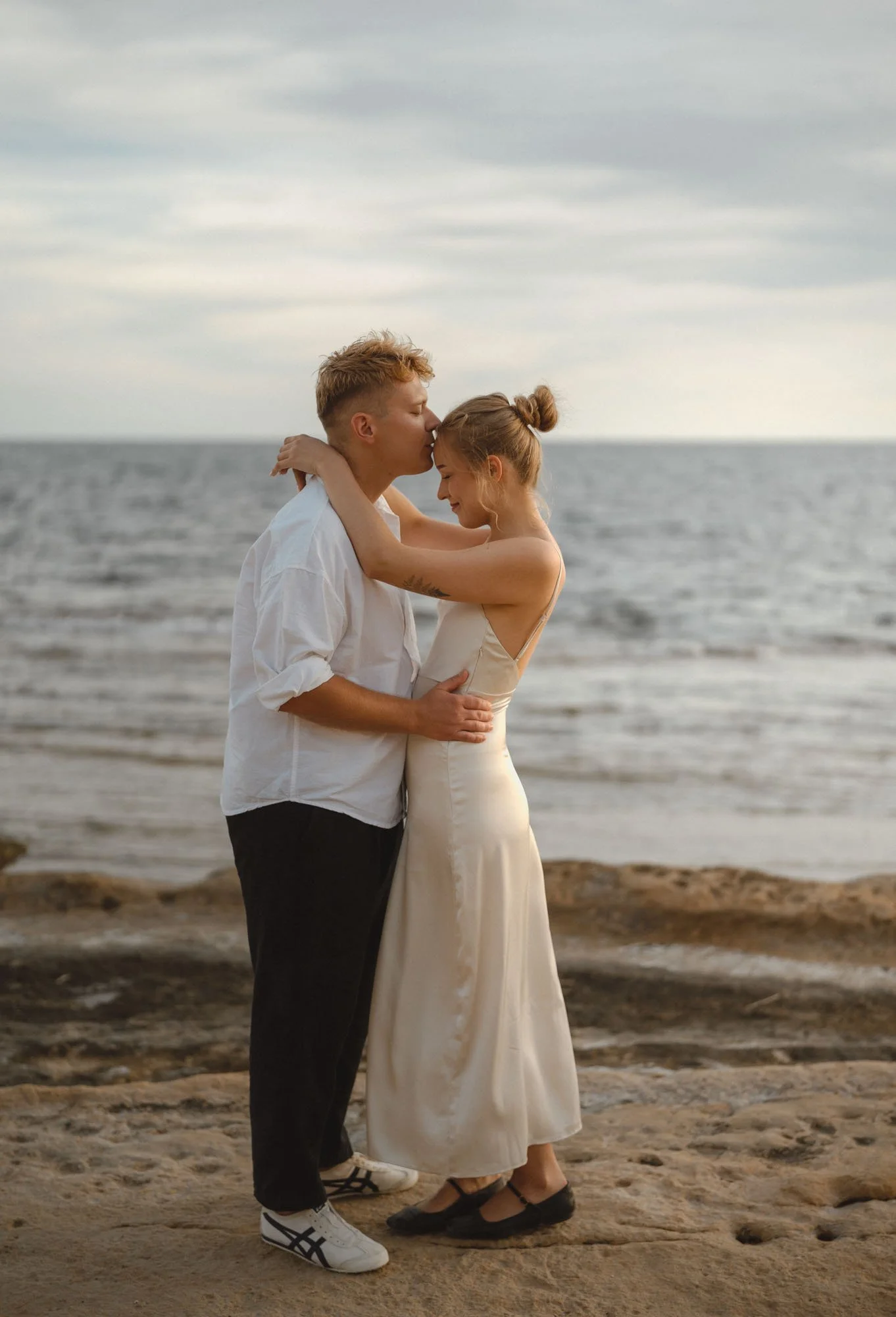 A young couple embracing on a beach, with the man kissing the woman's forehead, during sunset or early evening. Alicante, Cabo 
