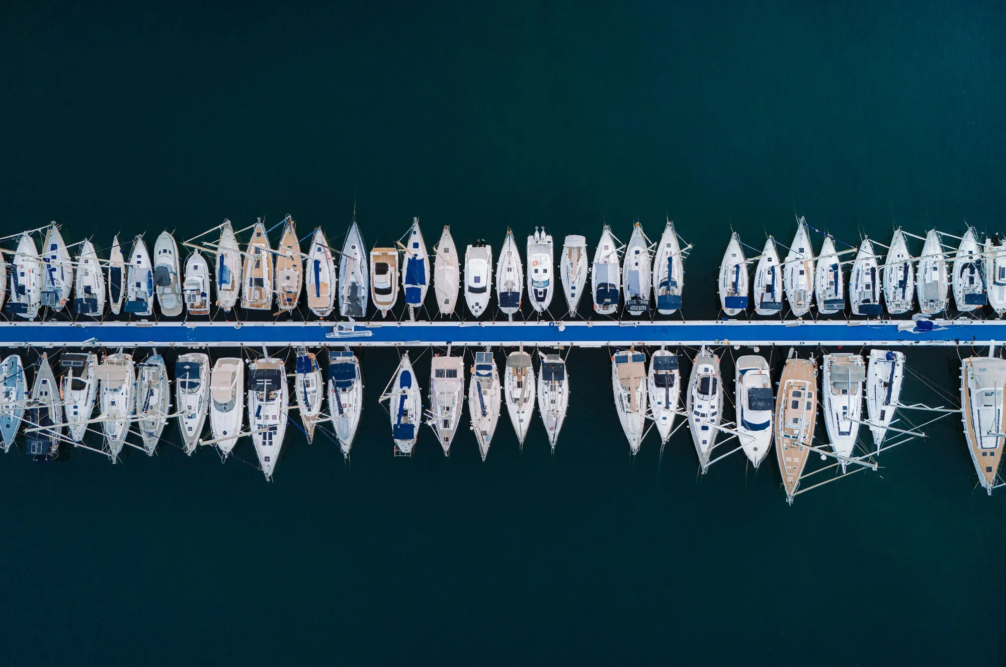 Overhead view of a marina with multiple boats docked on both sides of a floating pier.