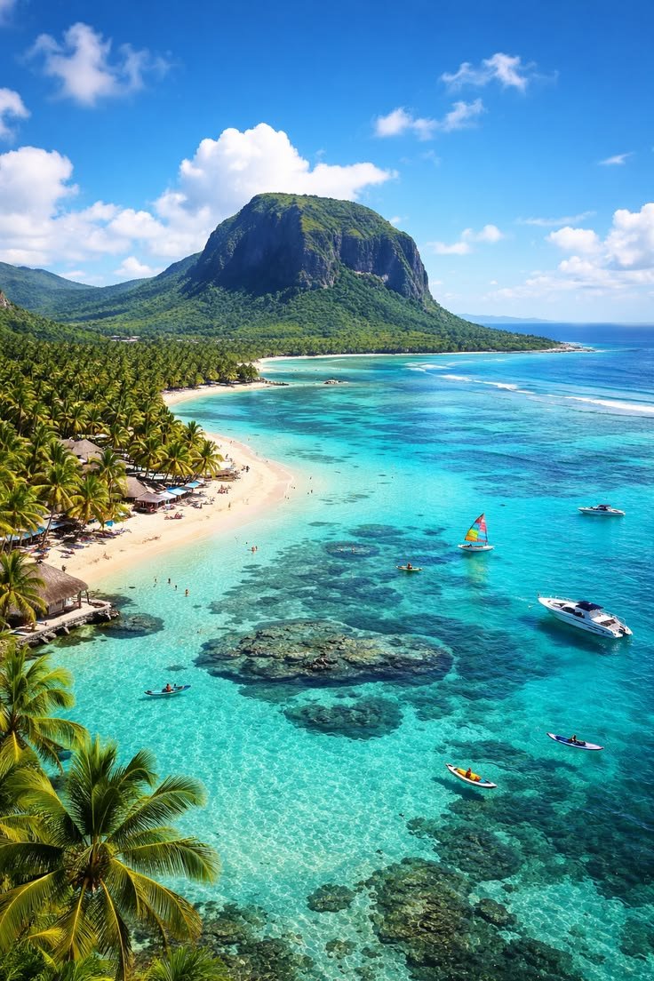 Plage tropicale avec palmiers, eaux turquoise, montagne verte en arrière-plan et bateaux sur l'eau.