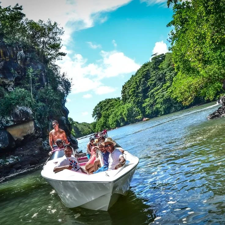 Groupe de personnes faisant du bateau sur une rivière entourée d'arbres verts sous un ciel bleu avec quelques nuages. C'est à l'île Maurice.