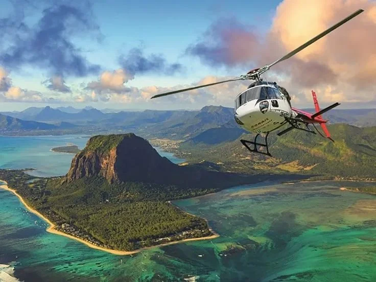 Hélicoptère volant au-dessus d'une île avec montagnes, plages et eaux turquoise. C'est à l'île Maurice.