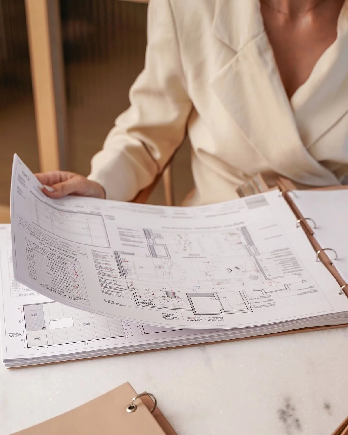 Persona revisando planos arquitectónicos en una mesa.