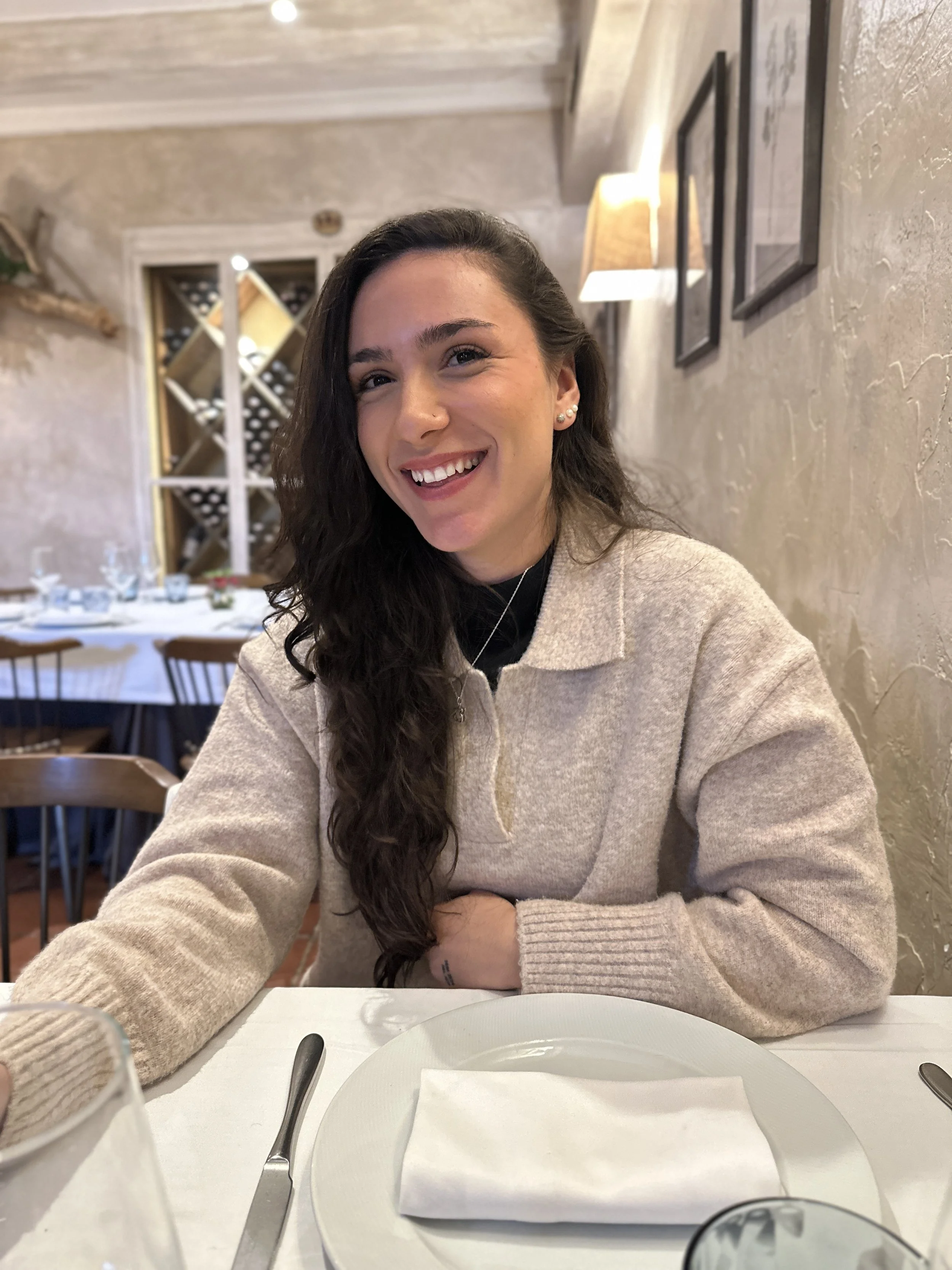 Mujer sonriendo con cabello largo y castaño oscuro, vestida con suéter beige.