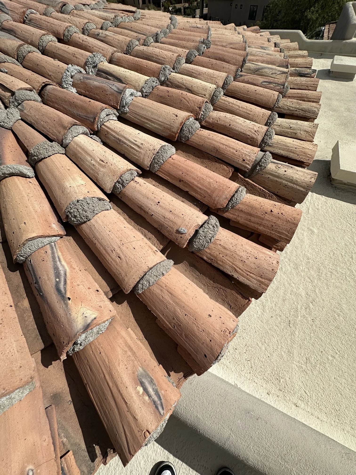 A rooftop with terracotta clay roof tiles stacked in rows, with some cement mortar visible between the tiles.