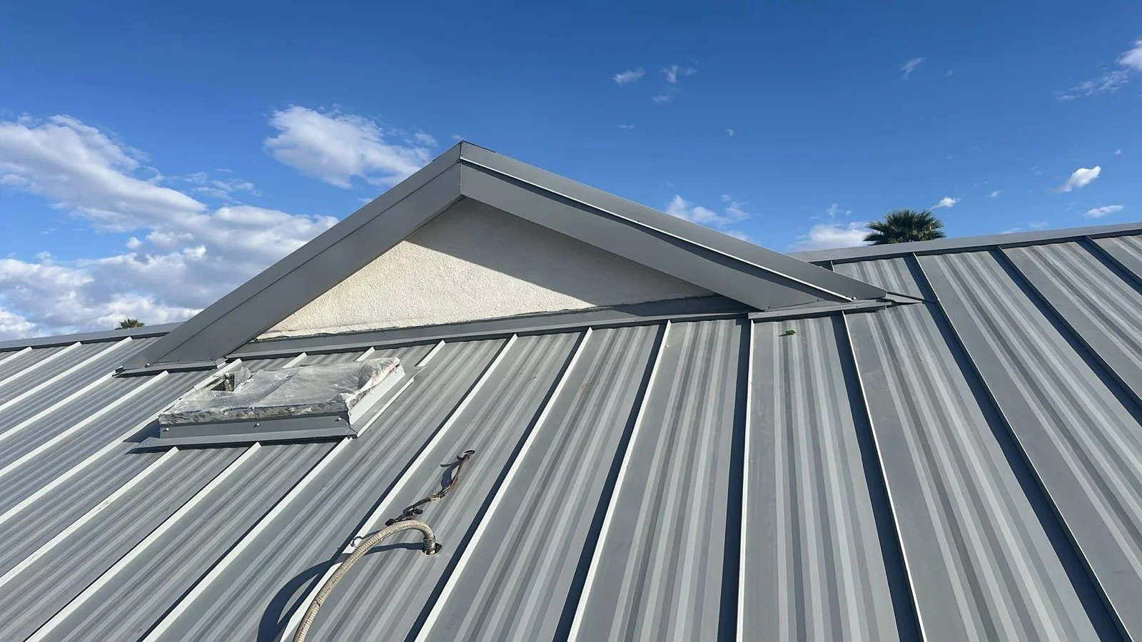 Close-up of a metal roof with a skylight and a vent on a sunny day with a blue sky and some clouds.