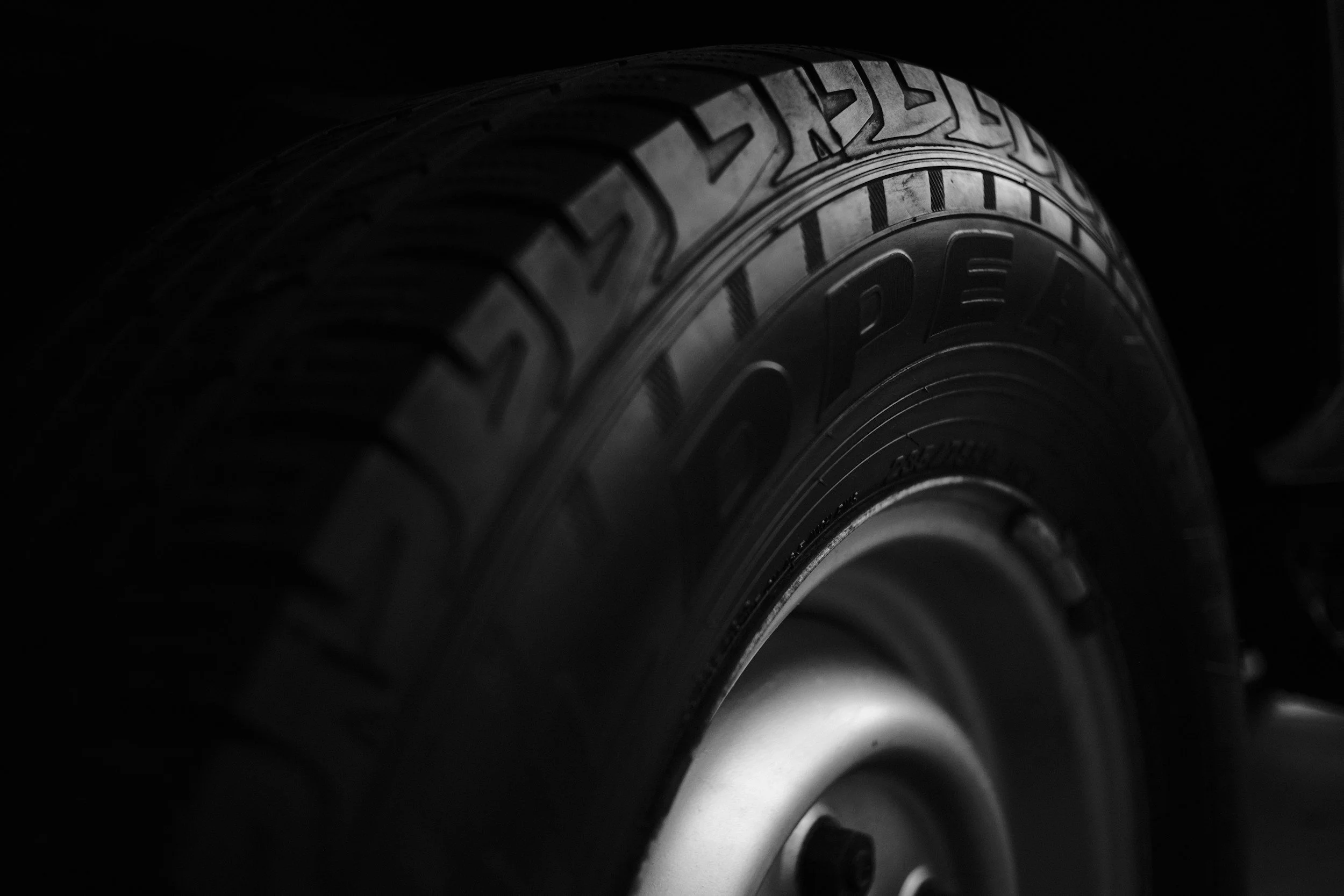 Close-up of a black tire with visible tread patterns, partially illuminated against a dark background.