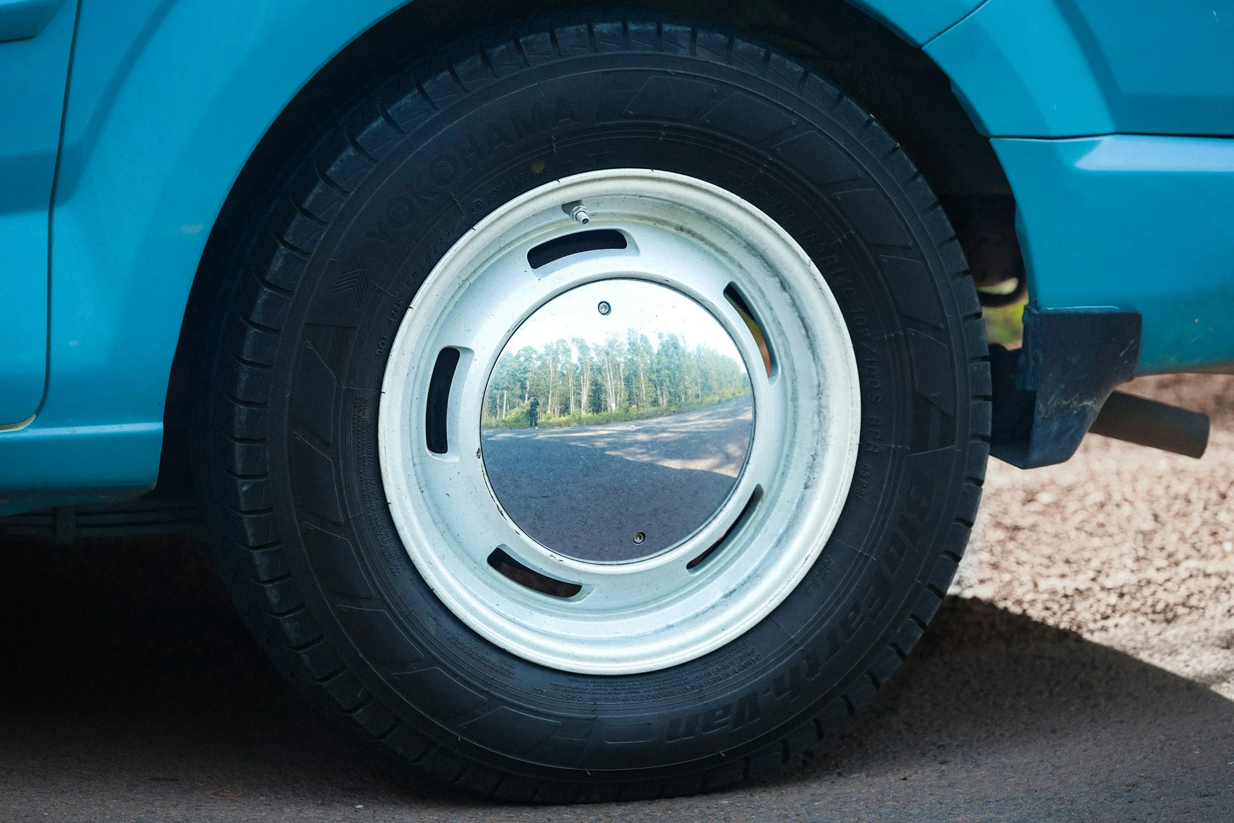 Close-up of a car wheel with a reflective hubcap showing a road and trees reflection.