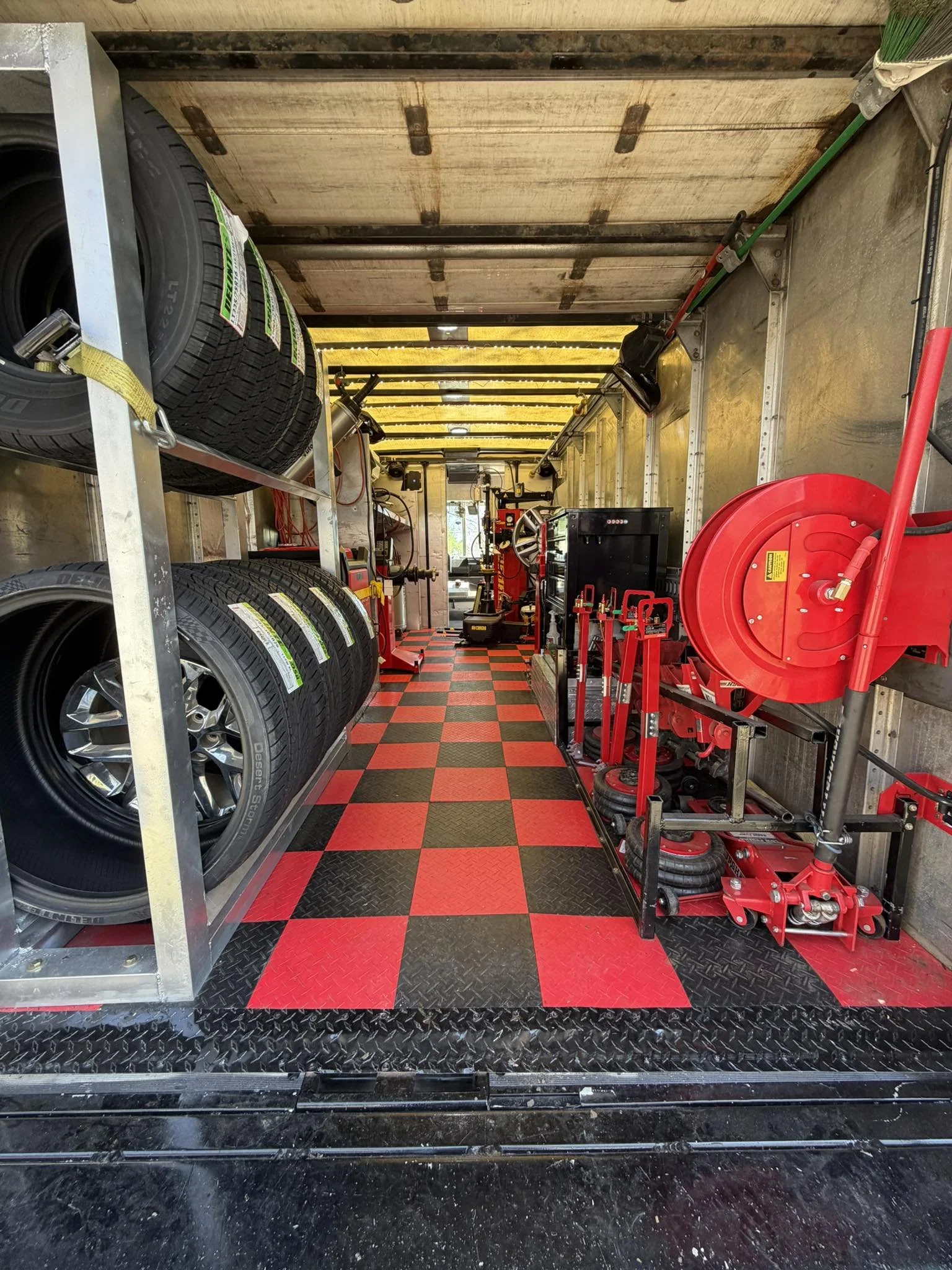 Interior of a mobile tire service truck with tires on the left, various tools and equipment on the right, and a checkered red and black floor.