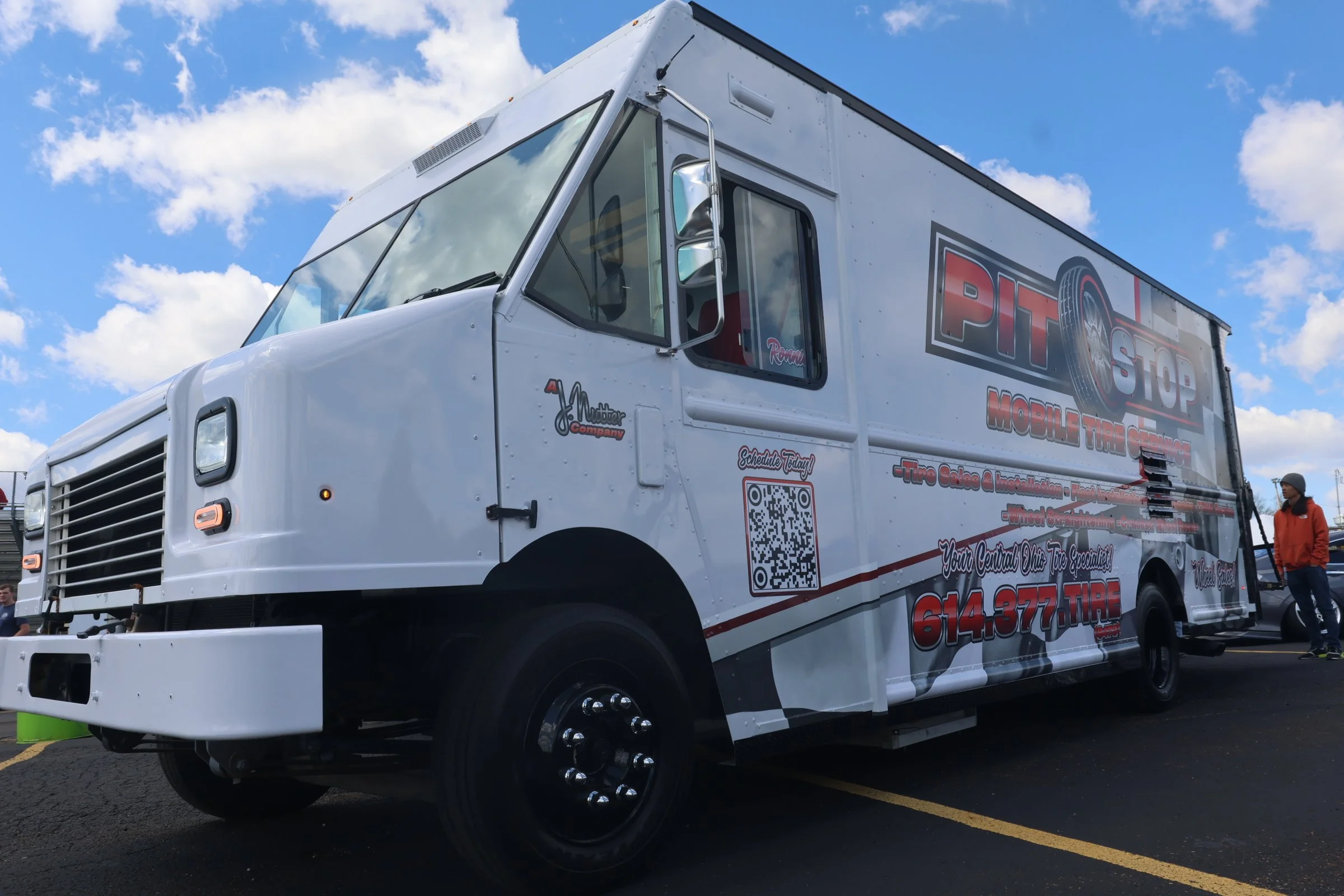 Mobile tire service truck parked outdoors with a person standing nearby, under a partly cloudy sky.