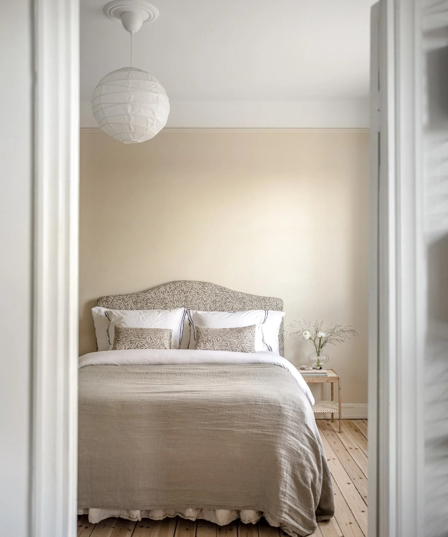 Stor styling av ljust sovrum i Stockholm med dubbelsäng, mönstrad sänggavel, mjuka textilier, belysning och genomtänkta detaljer