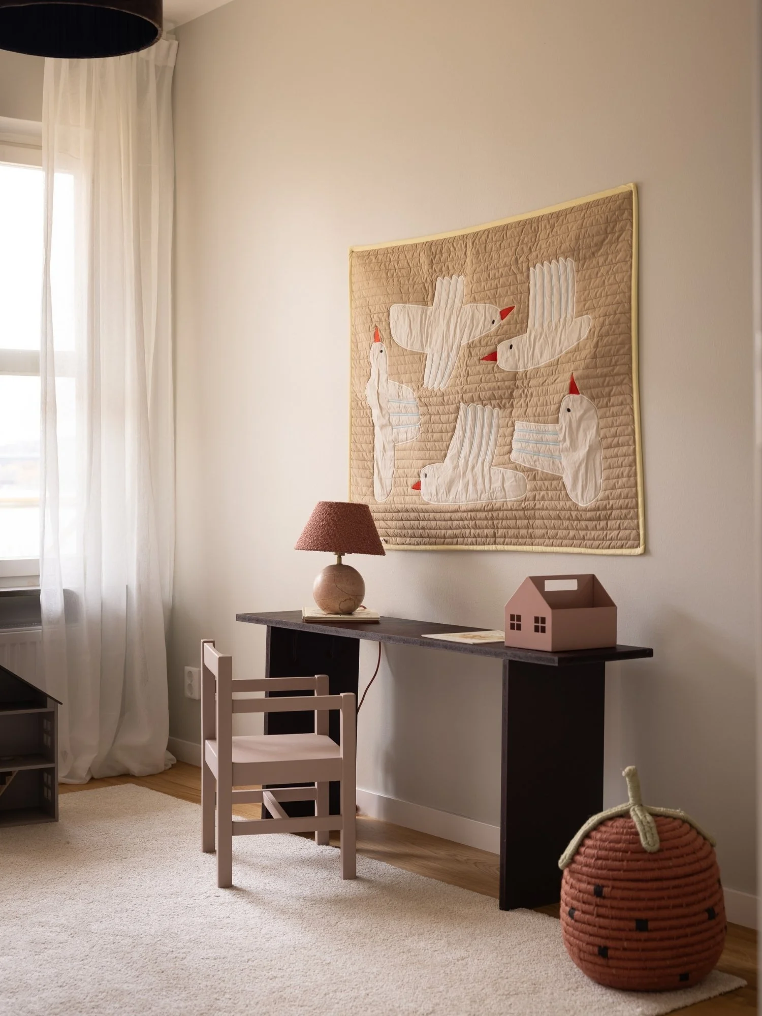 Skandinaviskt barnrum stylat med rosa stol, svart skrivbord, rosa detaljer och lager av mjuka textilier