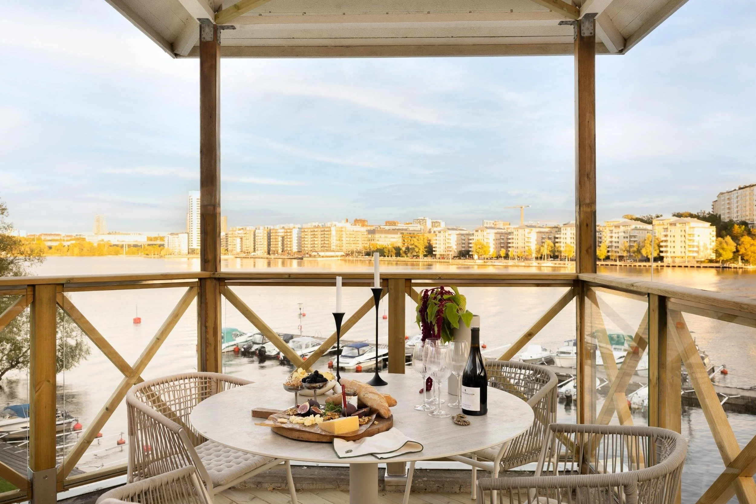 Uteplats med tak och havsutsikt samt vy över Kungsholmen i Stockholm, dukat bord med charkbricka, vinflaska, fyra vinglas, ljusstakar och vas med blommor